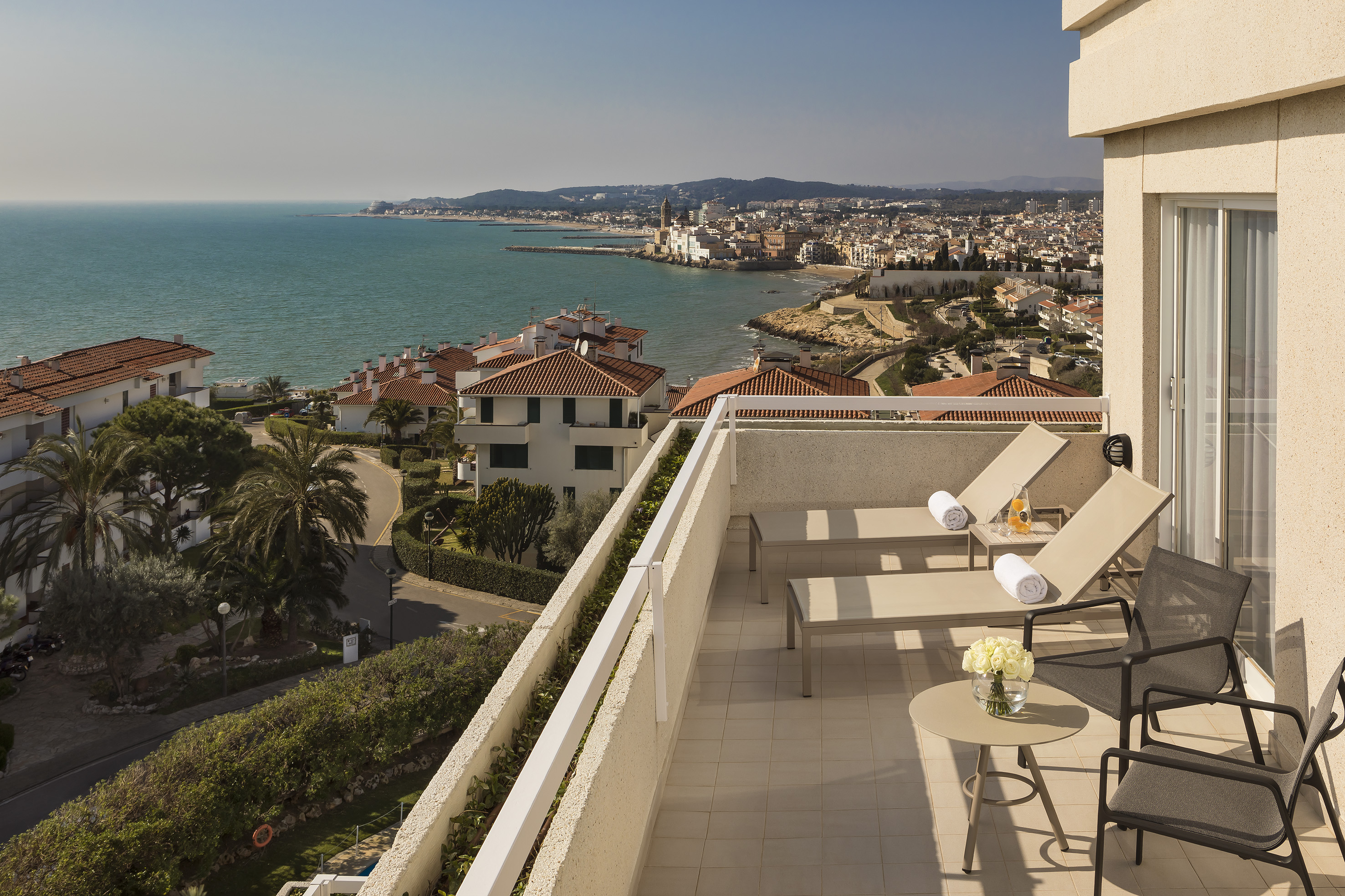 Balcony with lounge chairs, sea view, and Mediterranean coastal town.