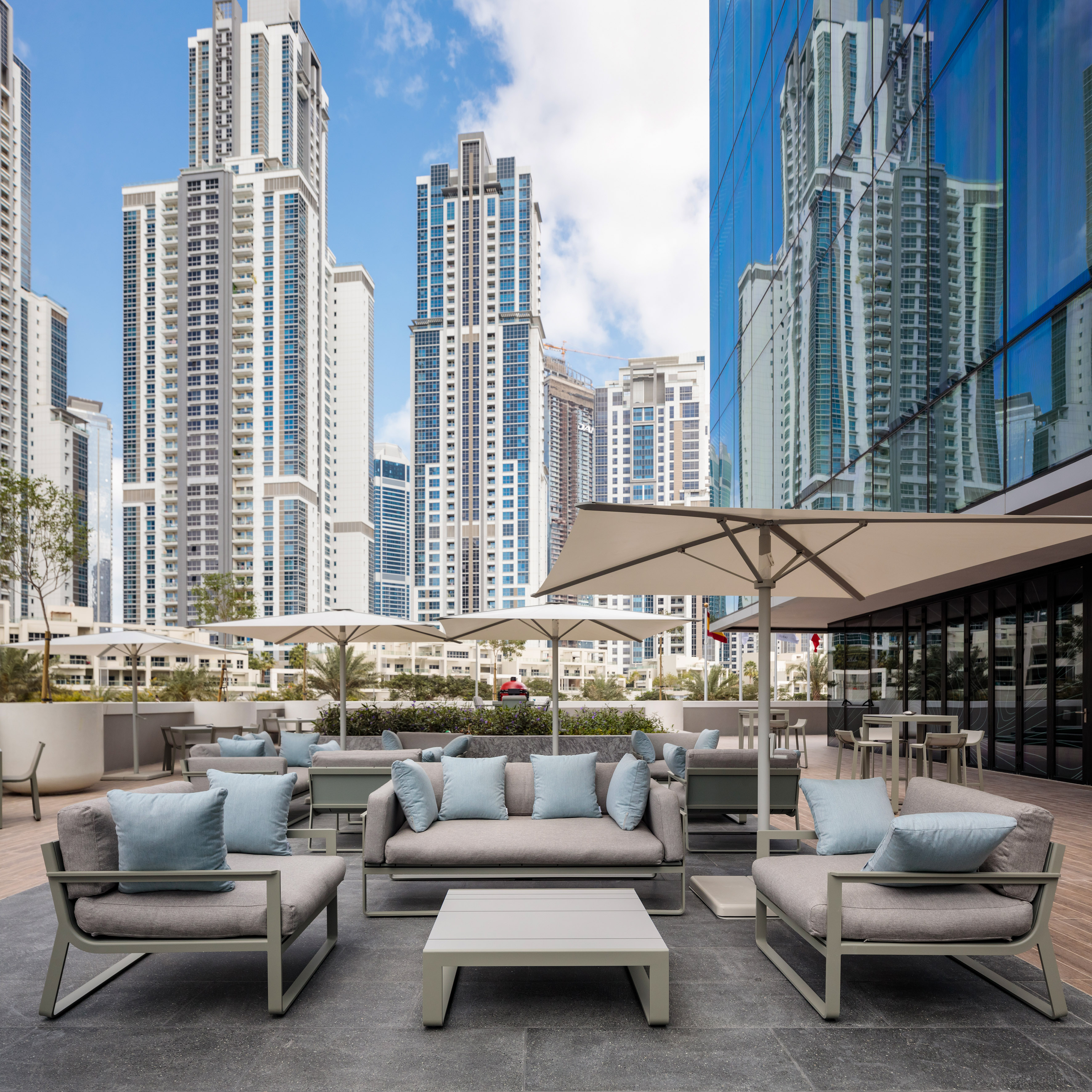 Modern outdoor lounge with grey seating, umbrellas, and urban skyscrapers.