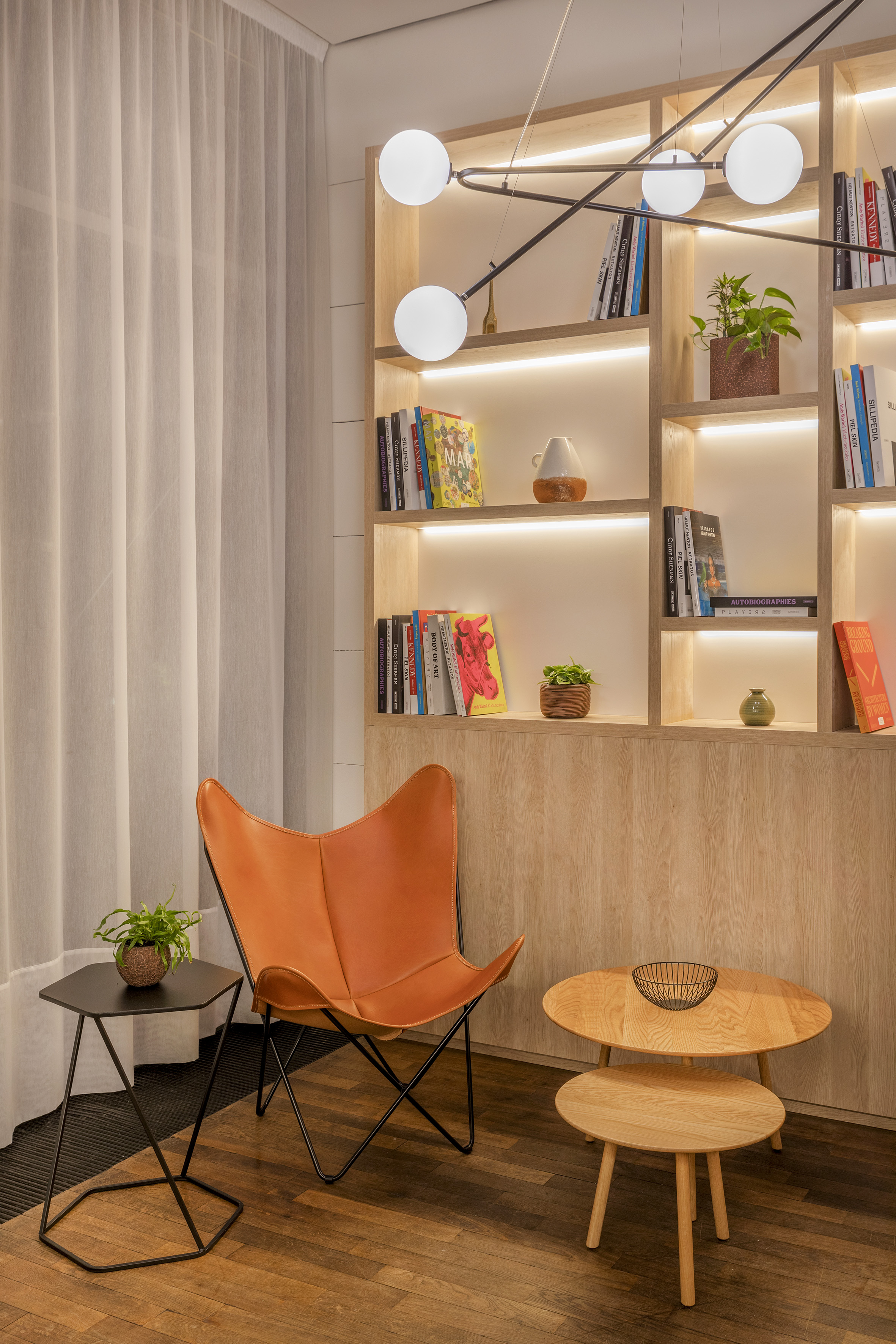 Modern living room with leather butterfly chair and illuminated wood bookshelf.