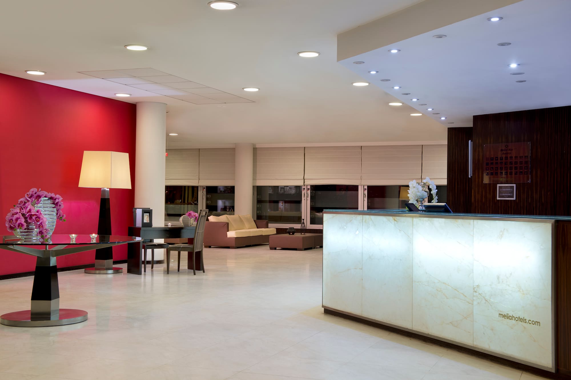 Modern hotel lobby featuring a glowing reception desk, red wall, and seating.
