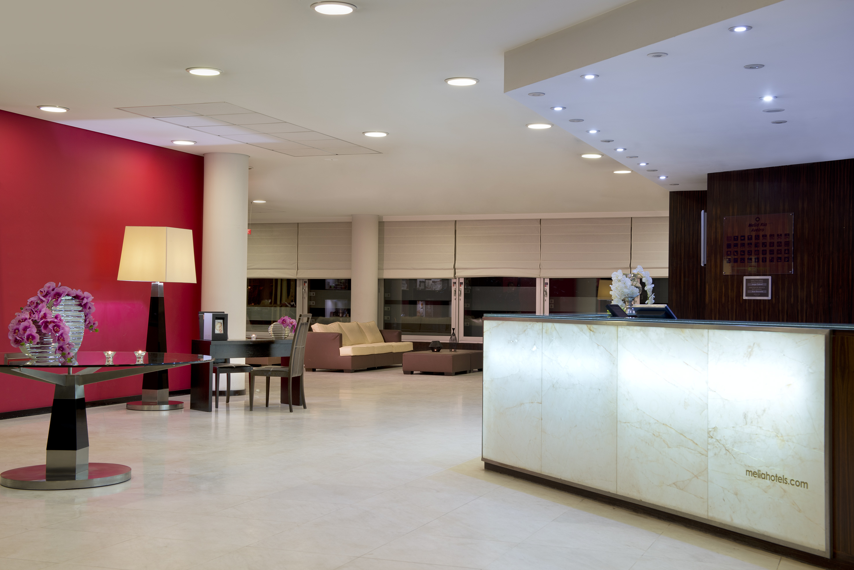 Modern hotel lobby featuring a glowing reception desk, red wall, and seating.