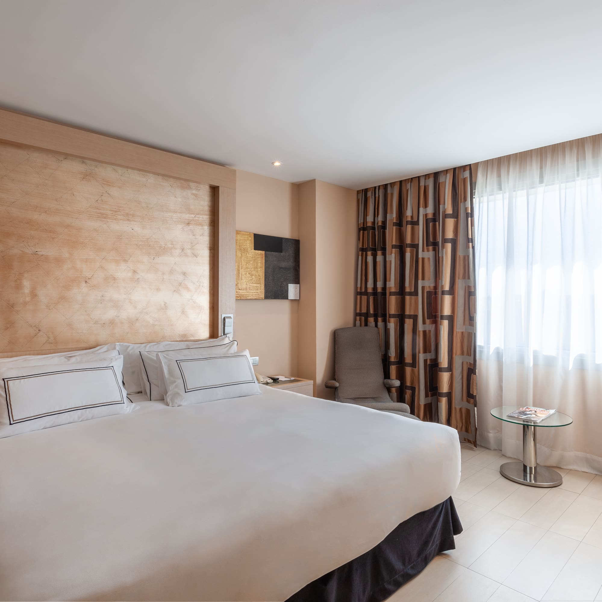 Modern hotel room with king bed, wood headboard, patterned curtains, and desk.
