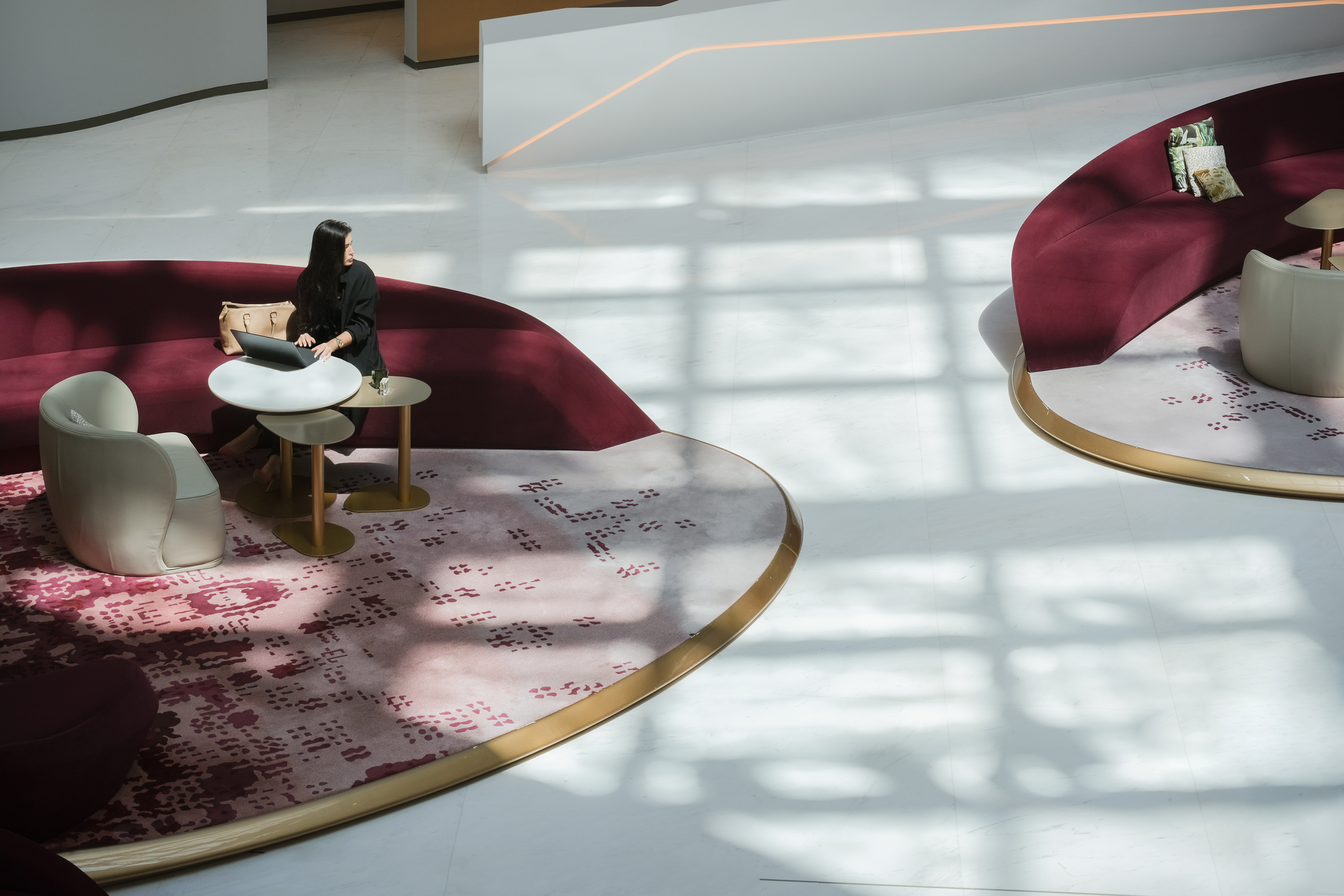 Woman working on laptop in modern hotel lobby lounge with burgundy sofa.