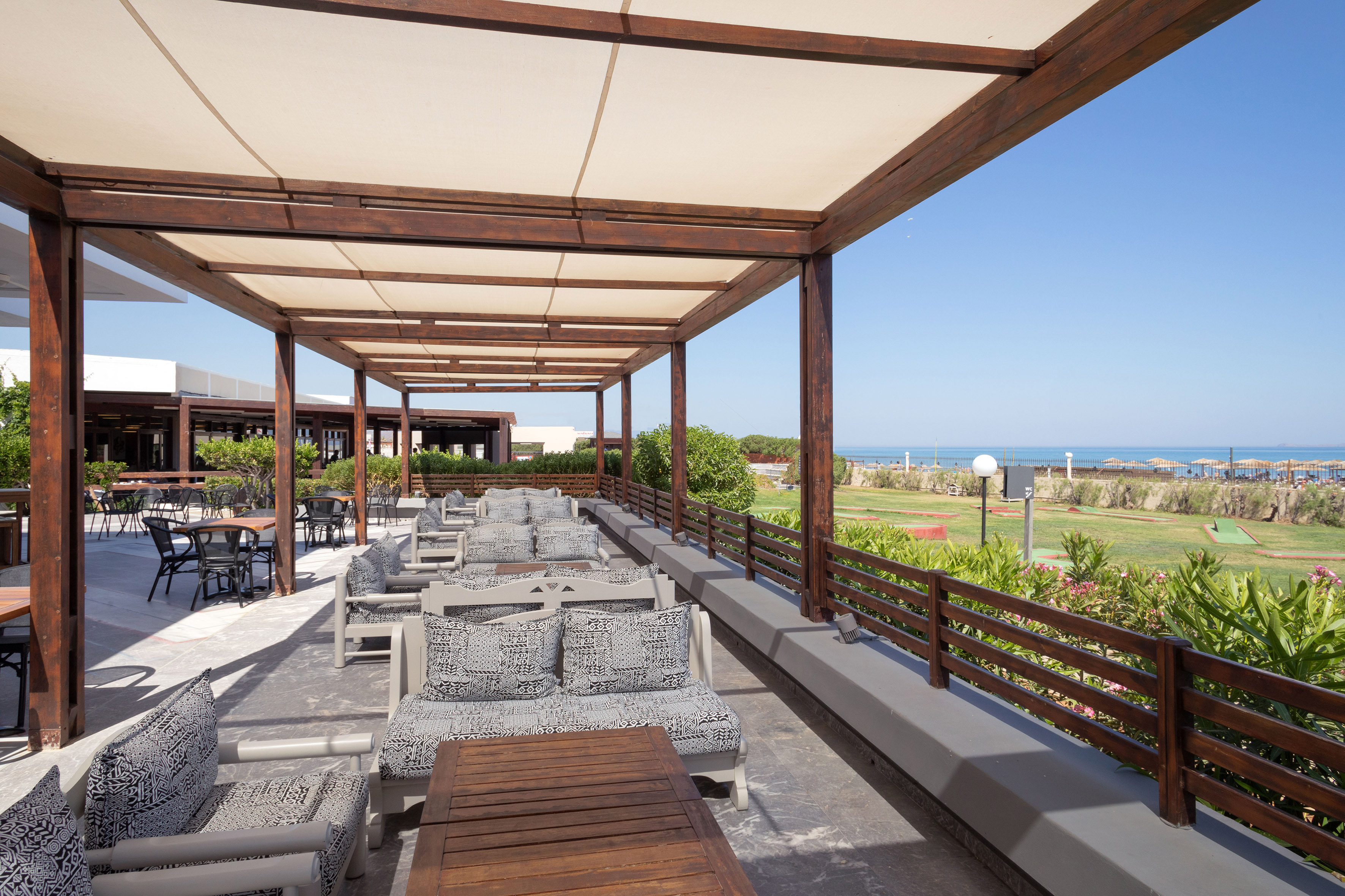 Expansive resort patio under pergola, featuring lounge seating and ocean views.