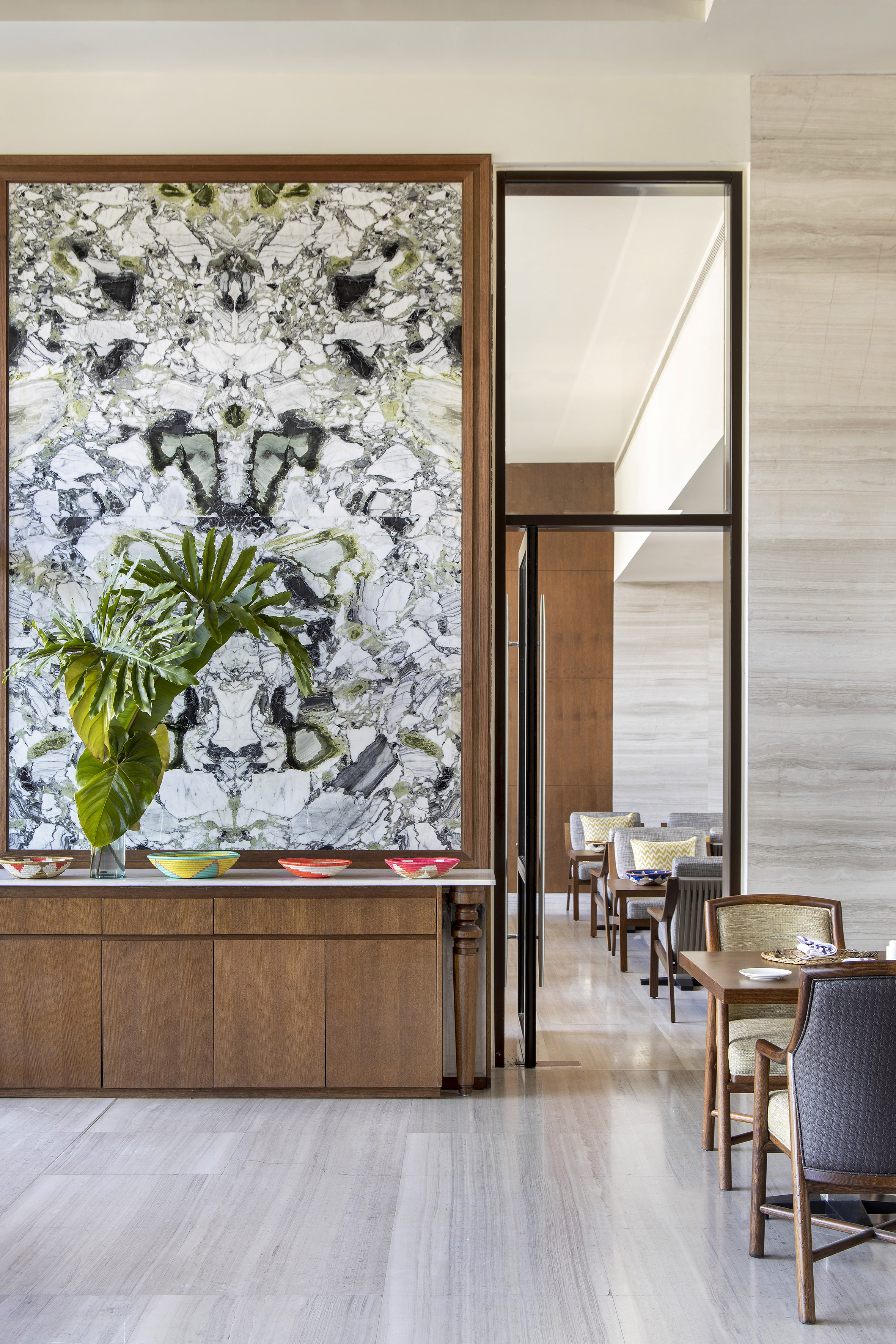Dining interior with large green marble wall, wood console, and green plants.
