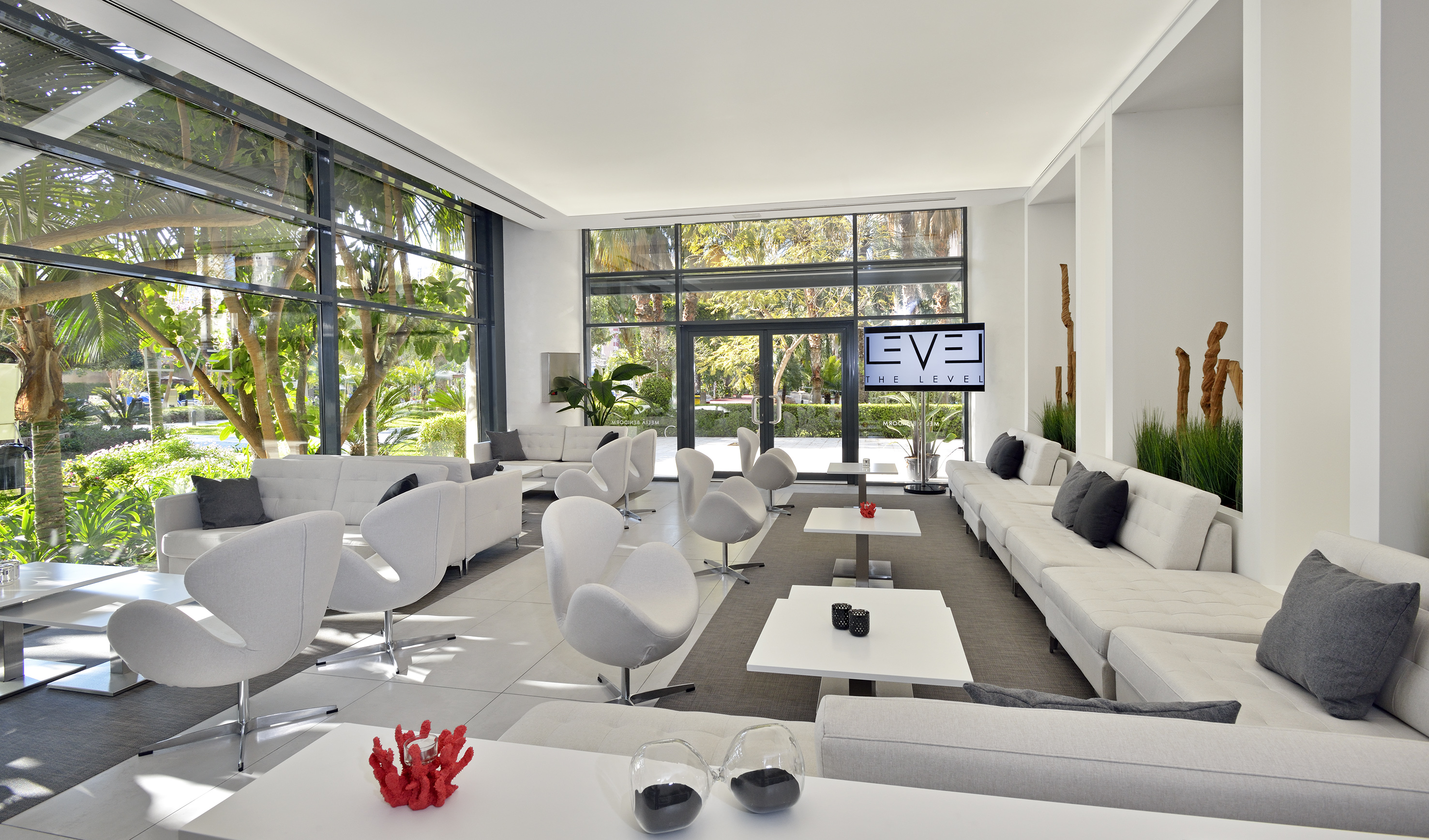 Modern lounge with white sofas, large windows, and tropical garden view.