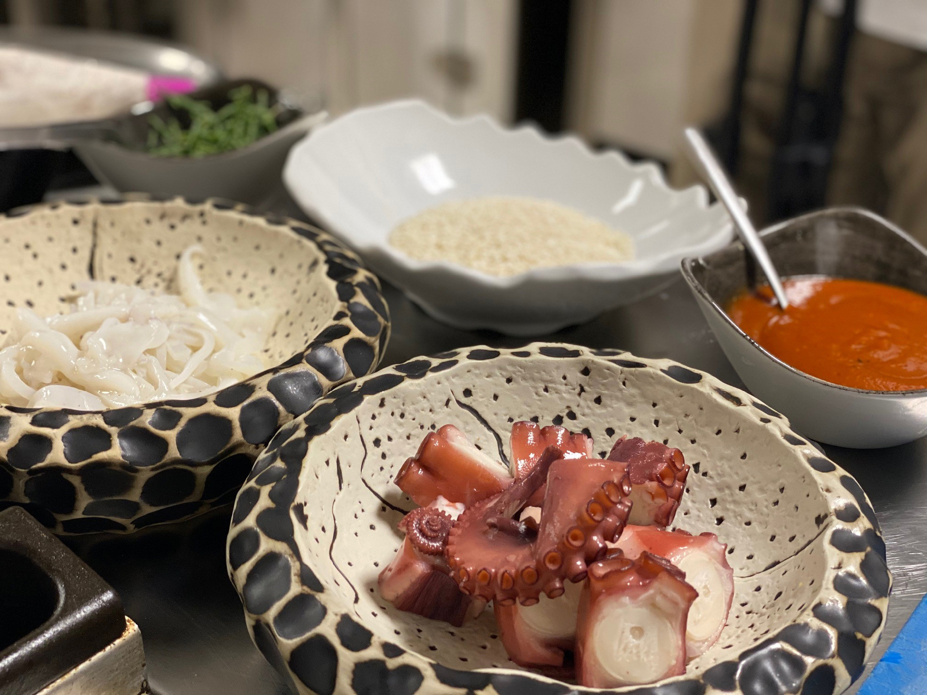 Prepared octopus, calamari, and tomato sauce in bowls for a seafood dish.
