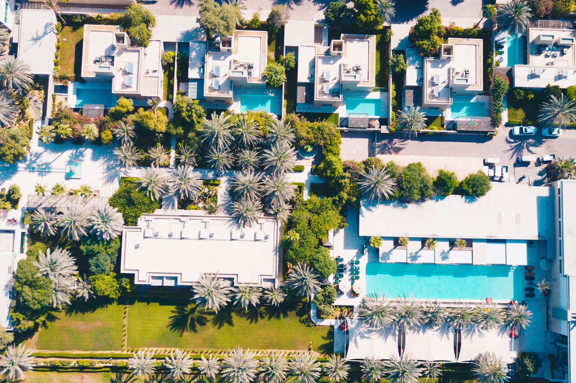 Aerial view: Luxury villas, pools, palm trees, and a vast green polo field.