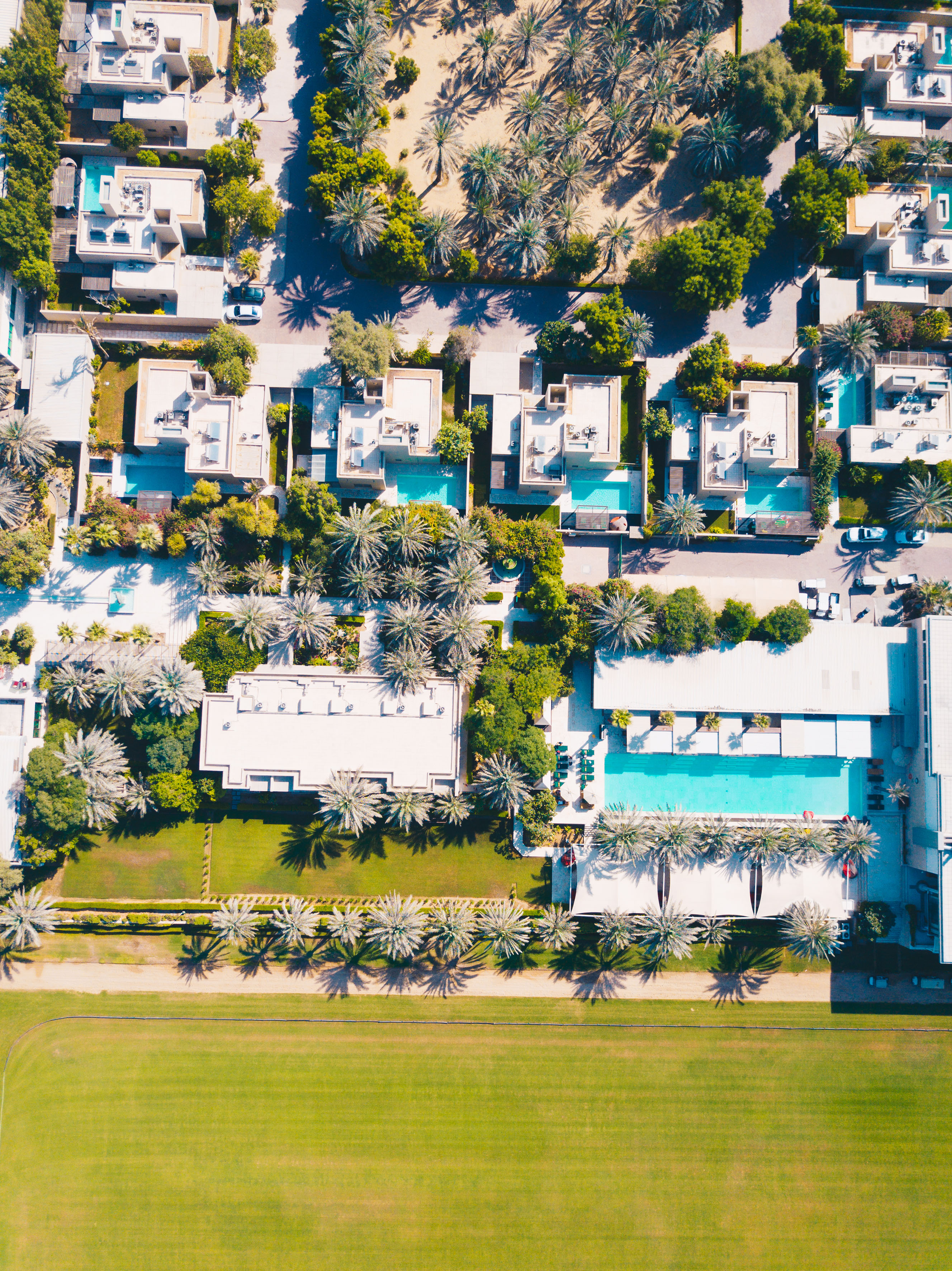 Aerial view: Luxury villas, pools, palm trees, and a vast green polo field.