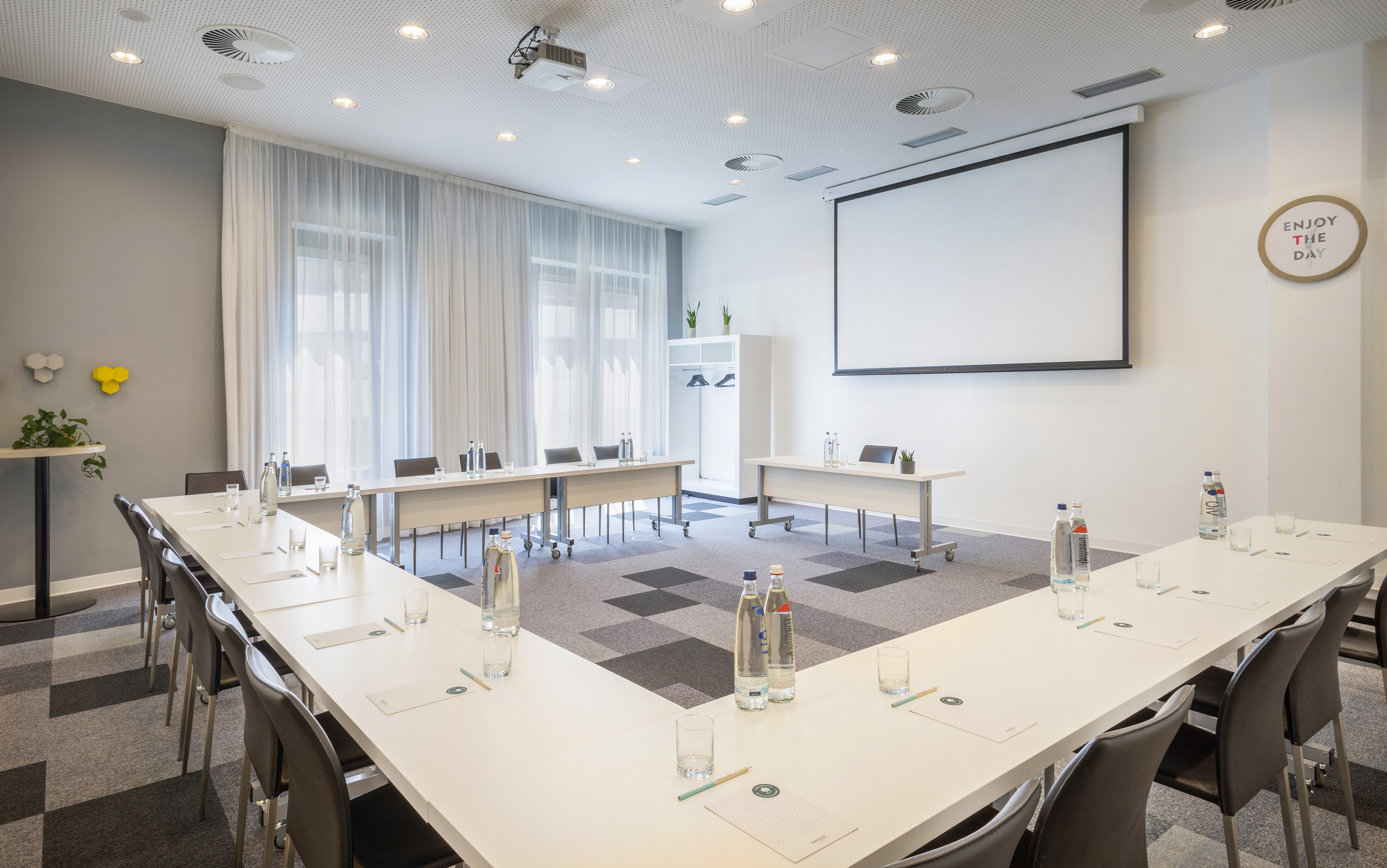 Modern U-shaped meeting room with projector screen, tables, and seating.