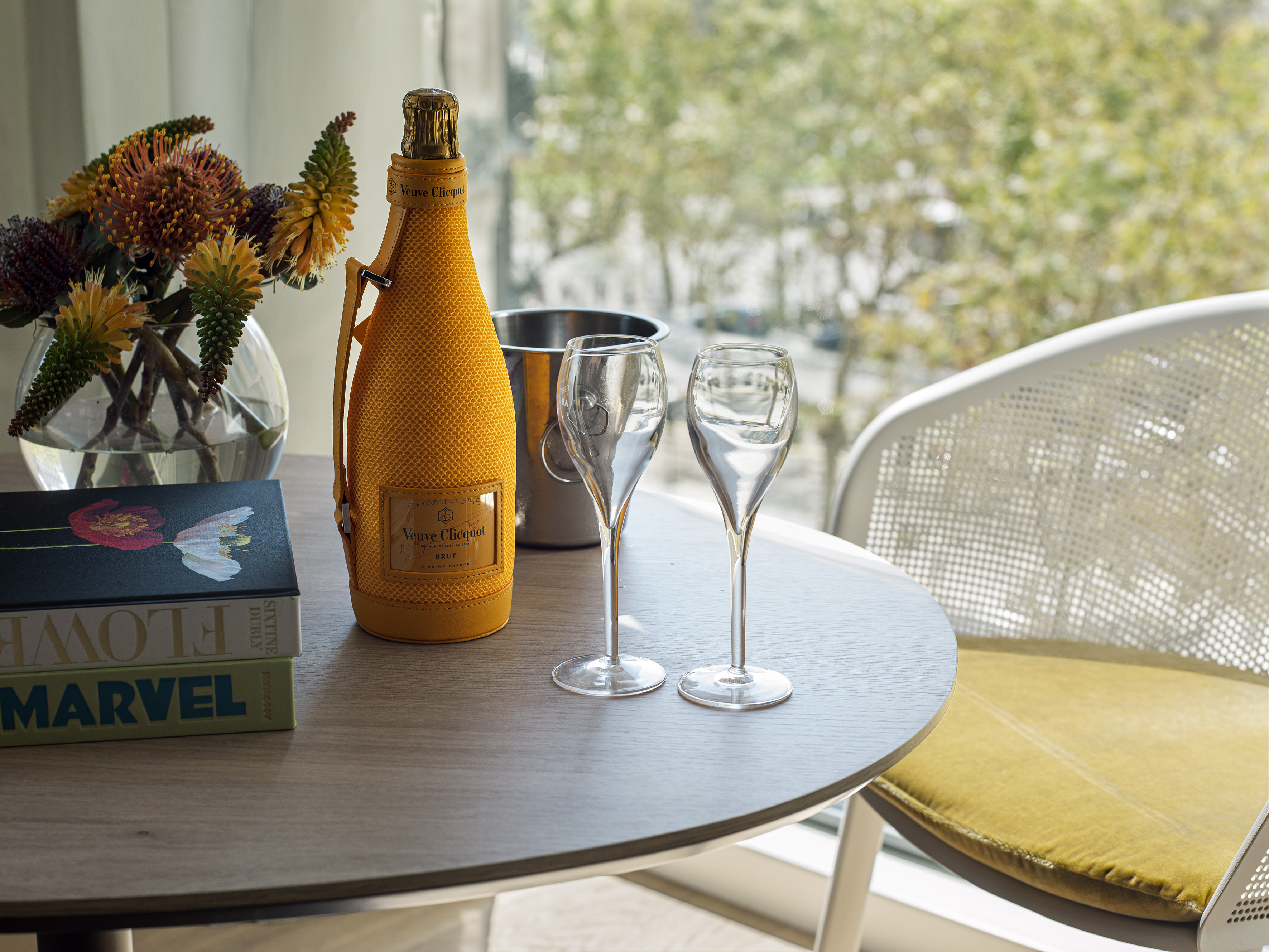 Yellow Veuve Clicquot champagne, flutes, and flowers on a wooden table.
