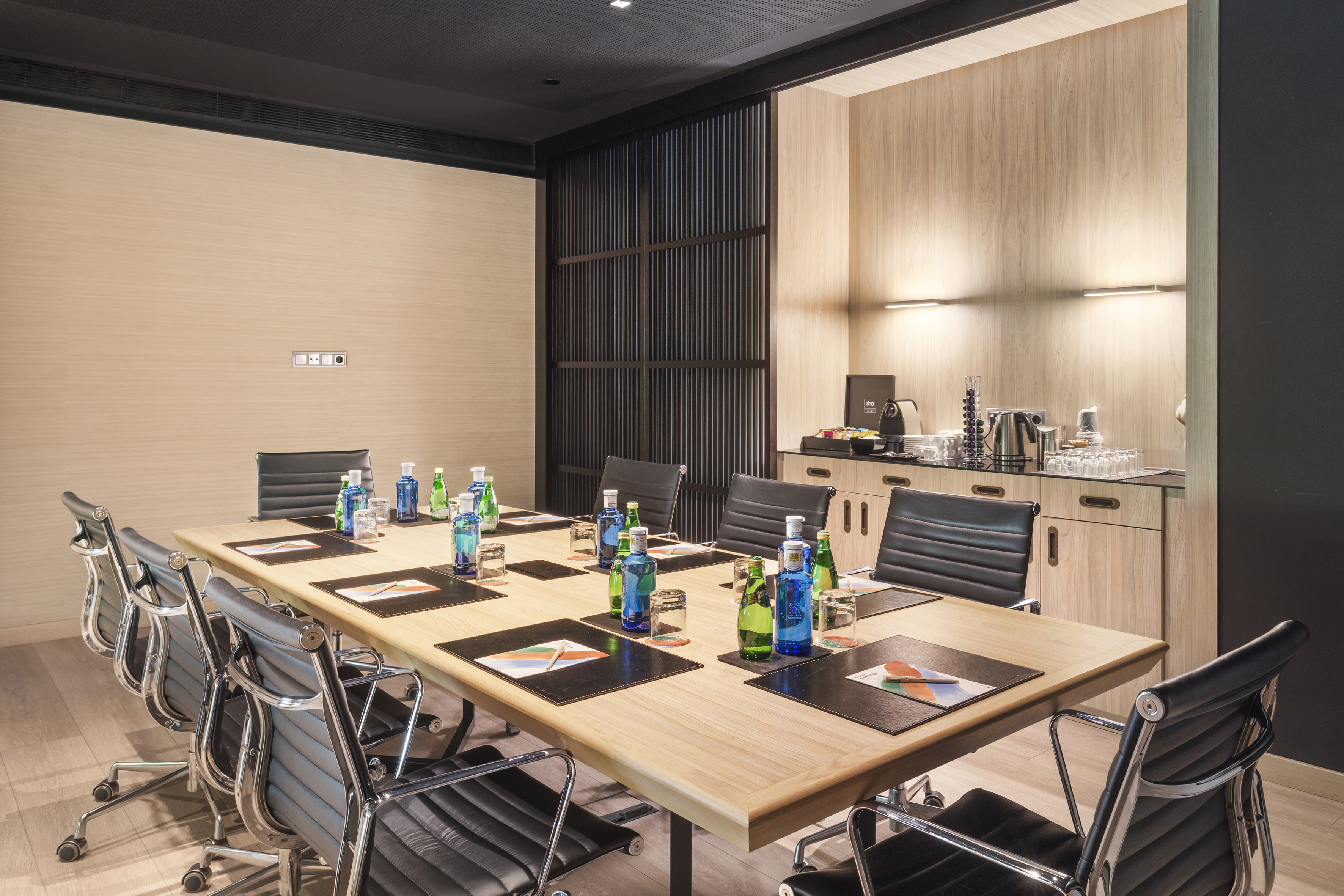 Contemporary meeting room with long table, leather chairs, and refreshment area.