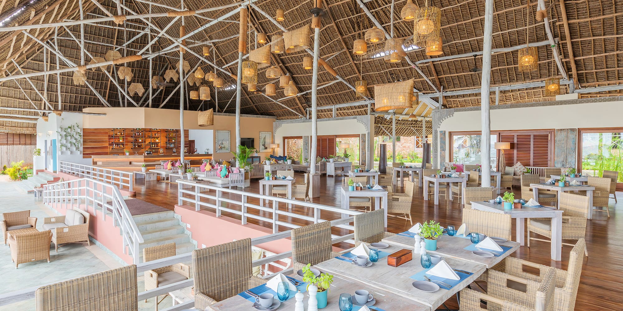 Tropical resort restaurant with high thatched roof, woven lights, and set tables.