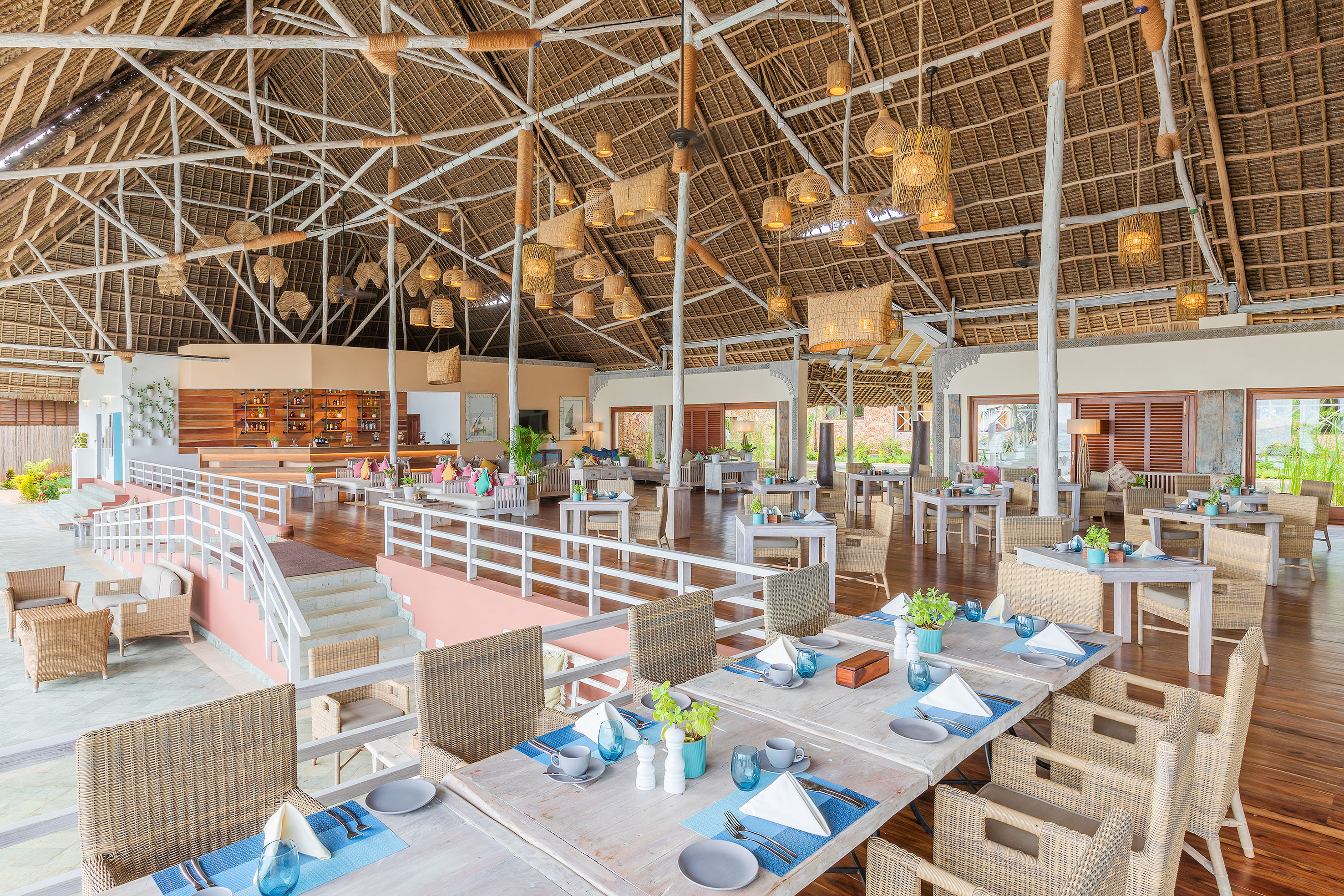 Tropical resort restaurant with high thatched roof, woven lights, and set tables.
