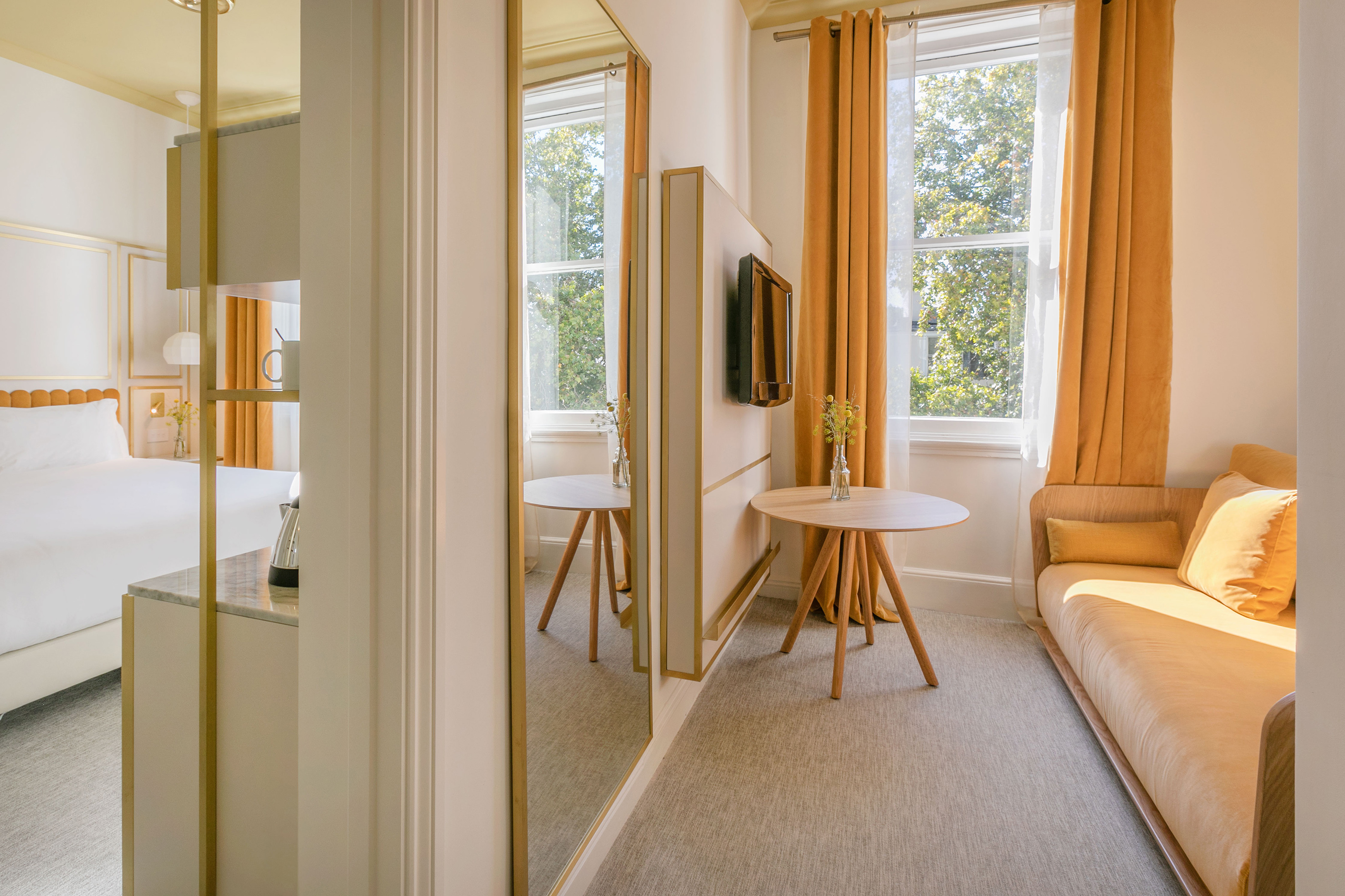 Modern hotel studio interior with bright windows, yellow curtains, sofa, and bed.