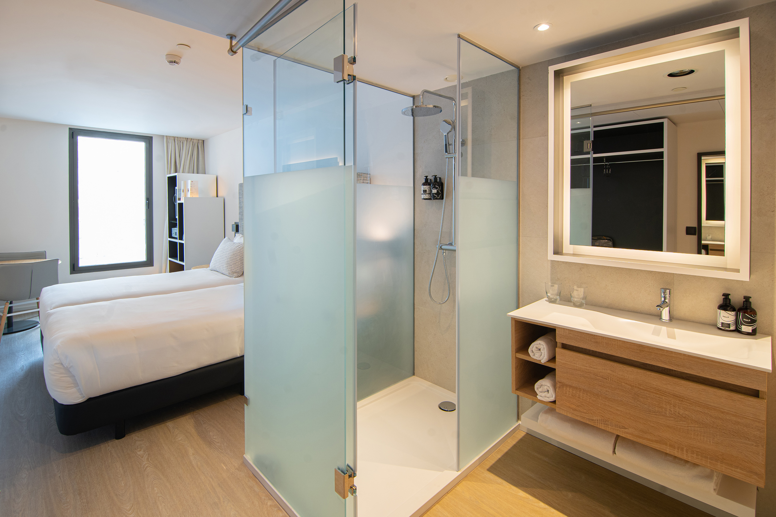 Modern hotel room: twin beds, walk-in shower, and illuminated vanity.