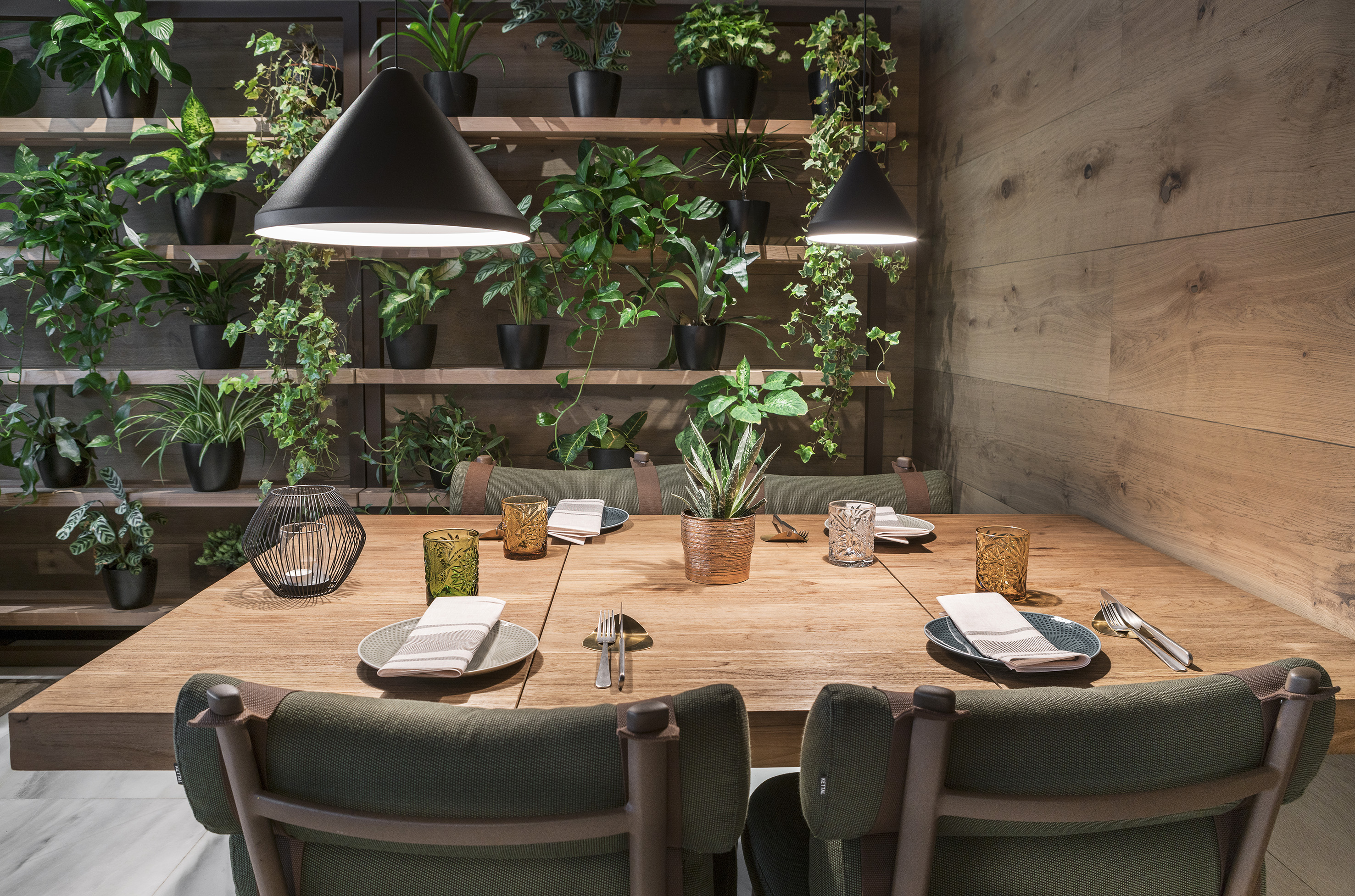 Modern dining table with lush plant wall and green chairs.