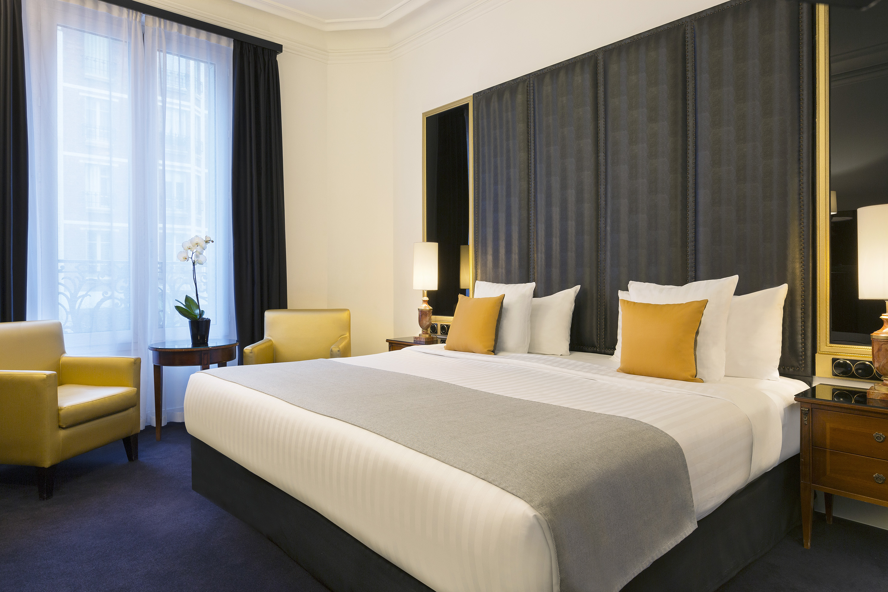 Elegant hotel bedroom with spacious bed, yellow accents, and dark headboard.