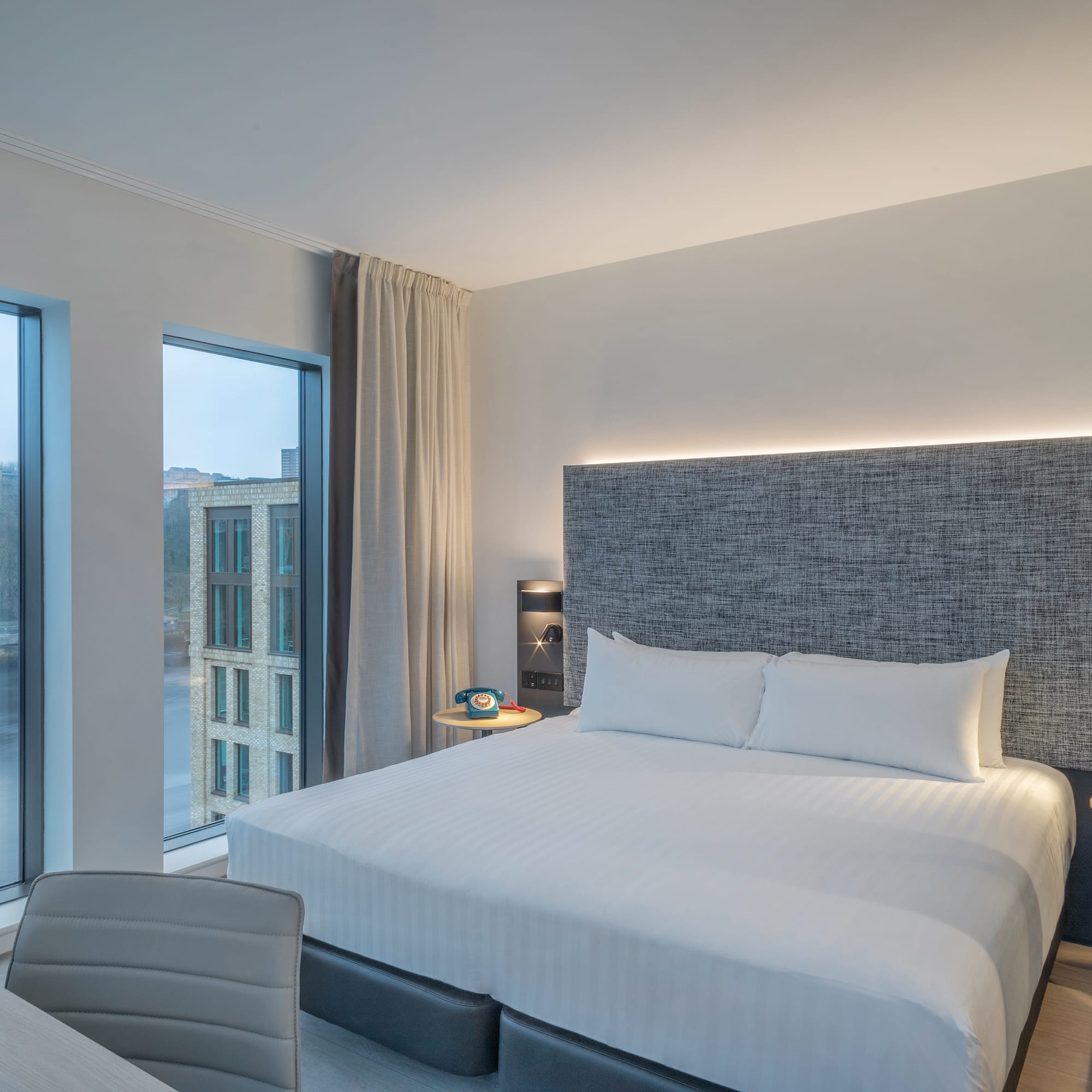 a bed with a headboard and a chair in a room with windows