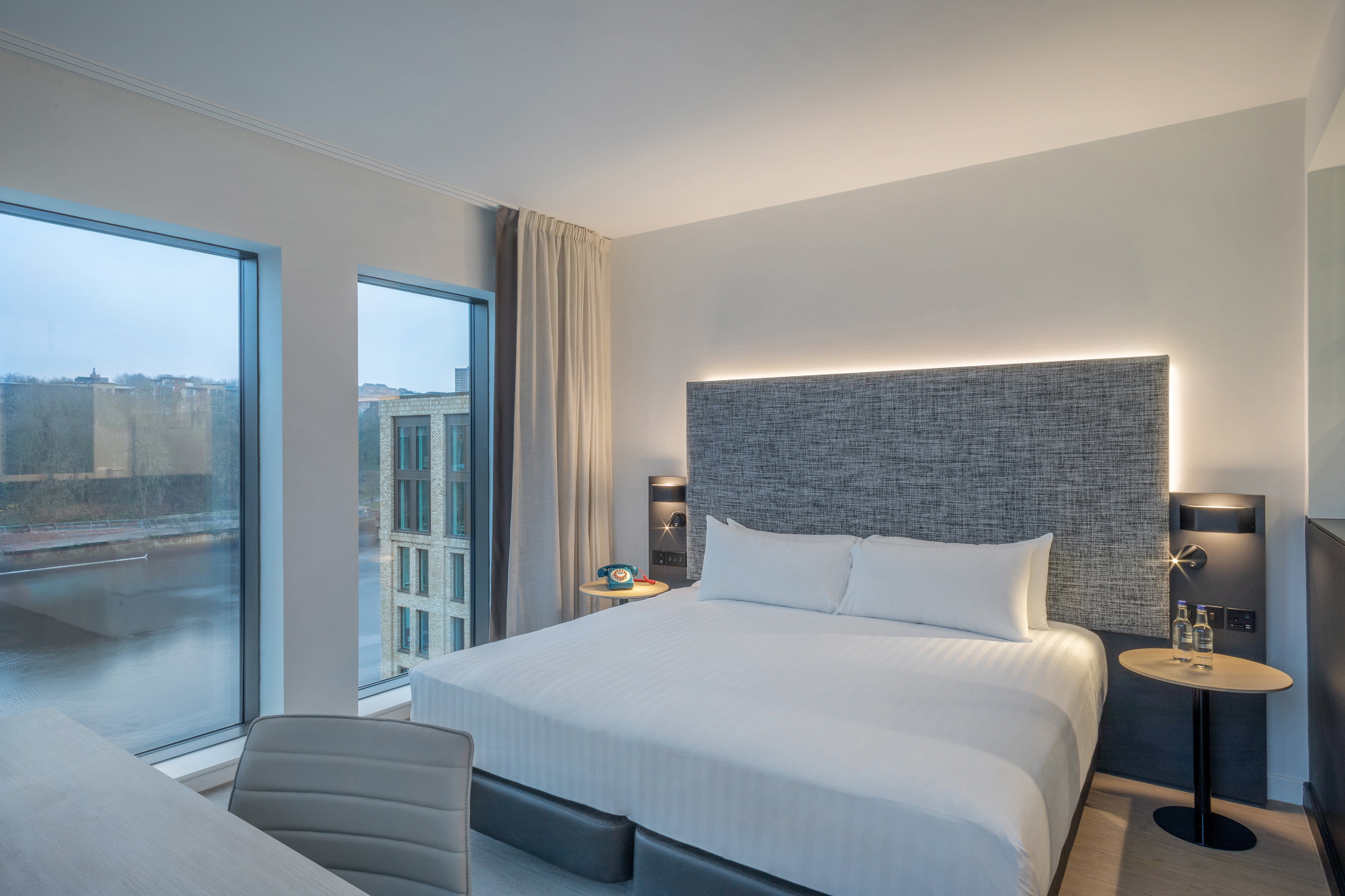 a bed with a headboard and a chair in a room with windows