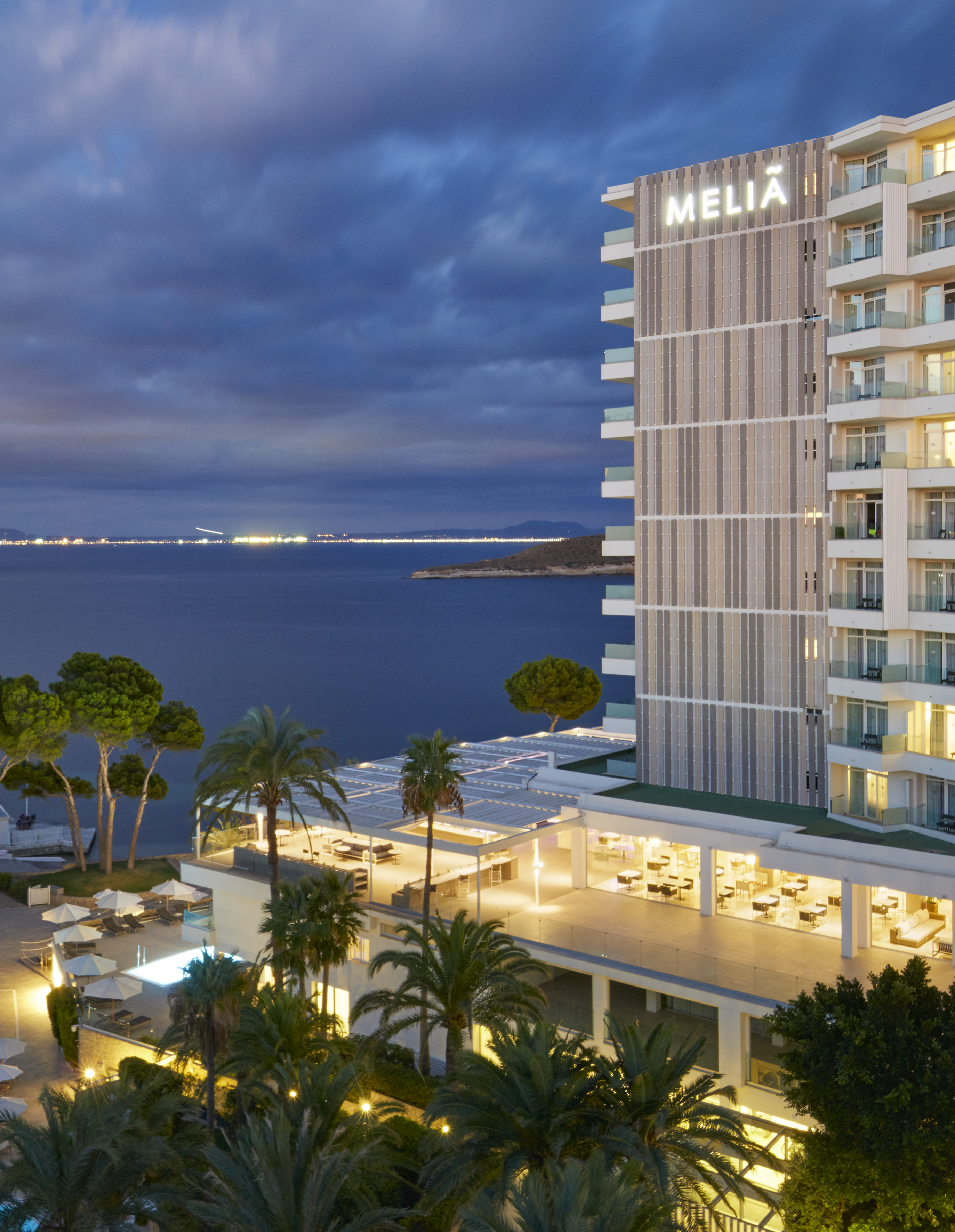 Melia Hotel at night, oceanfront with illuminated building and palm trees.