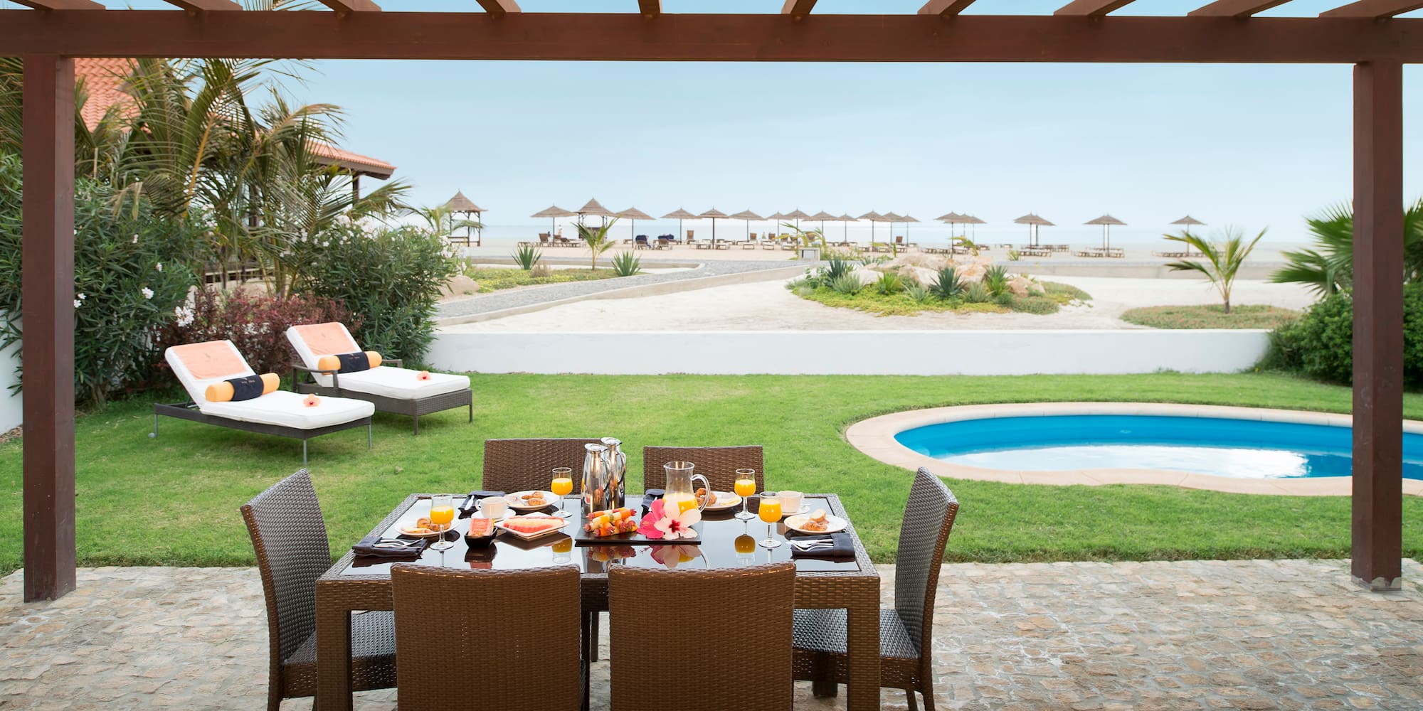 a table set for a meal outside with a pool in the background