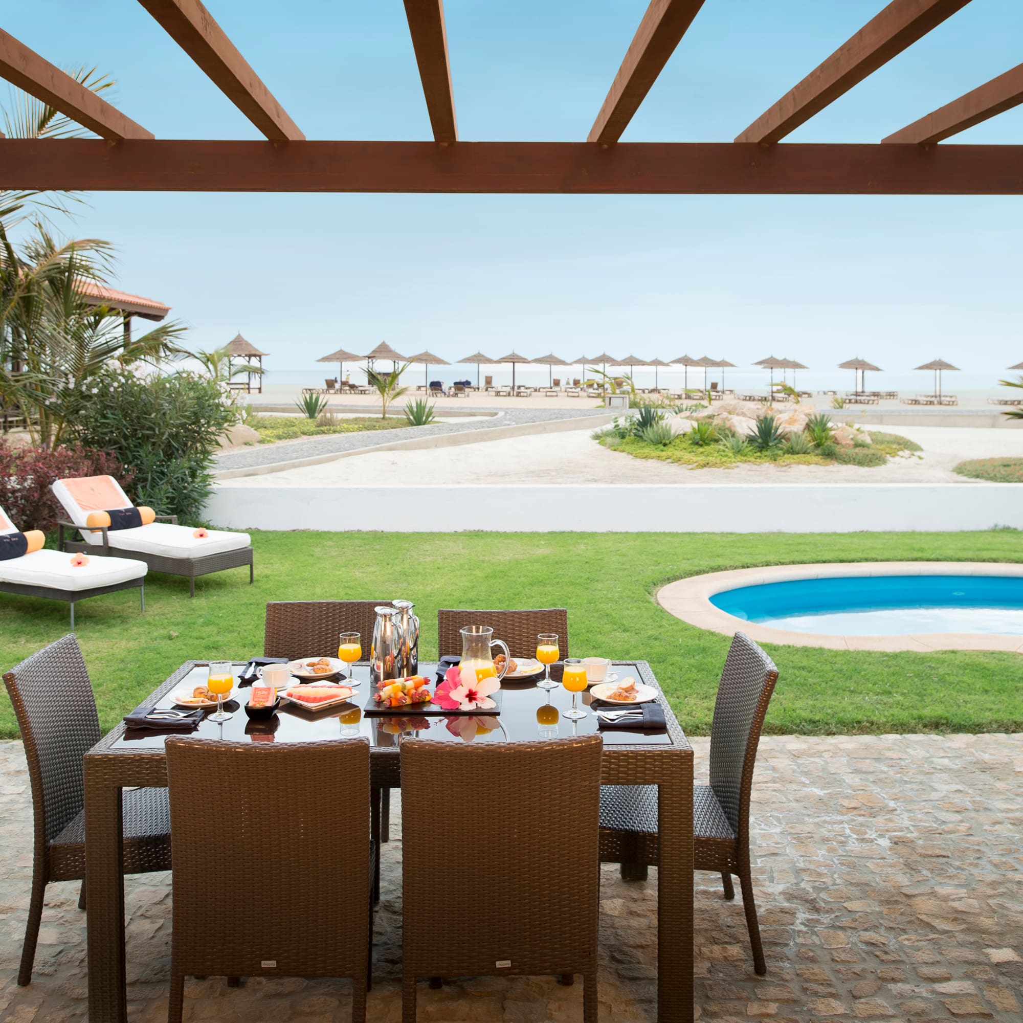 a table set for a meal outside with a pool in the background