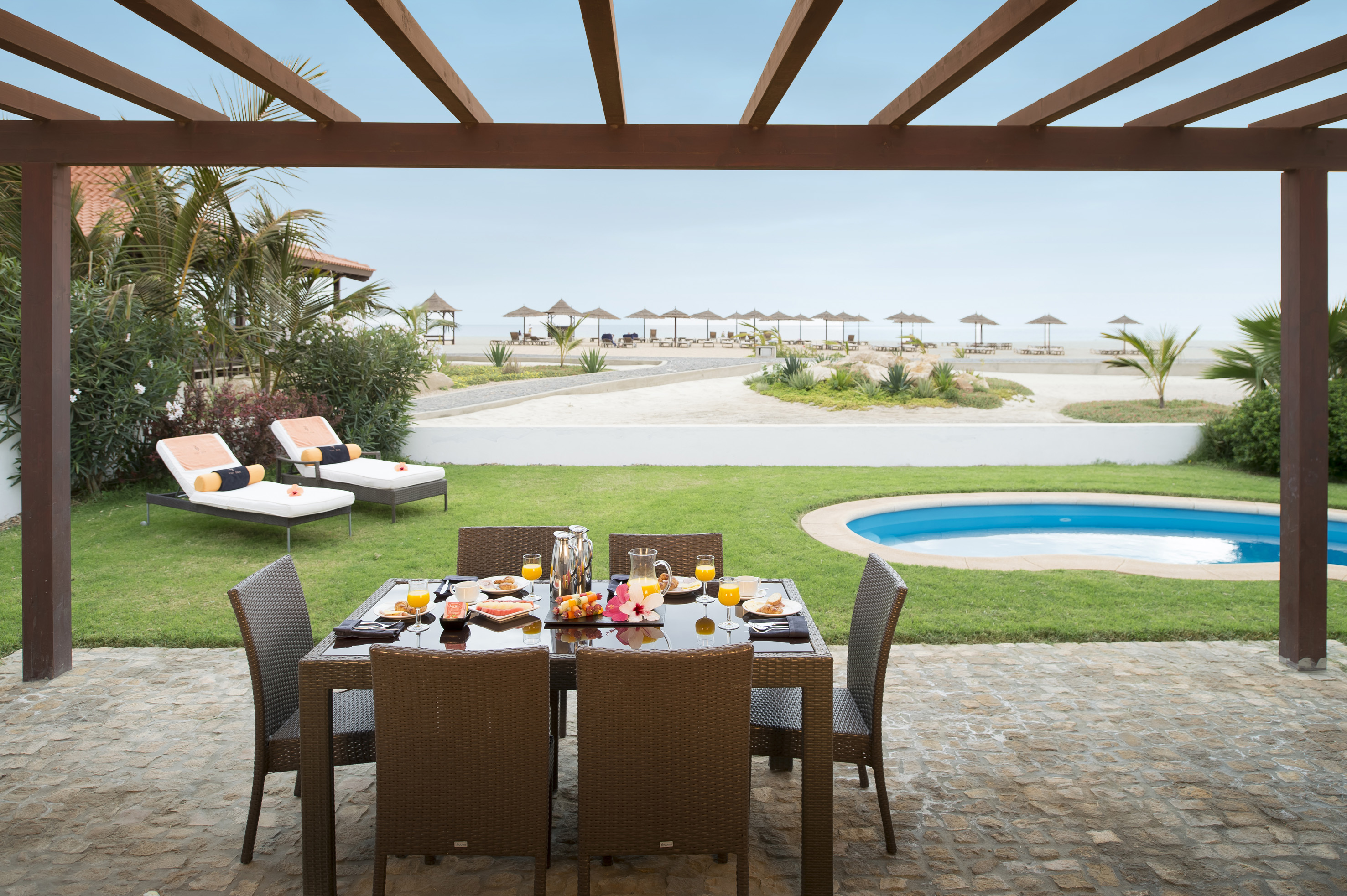 a table set for a meal outside with a pool in the background
