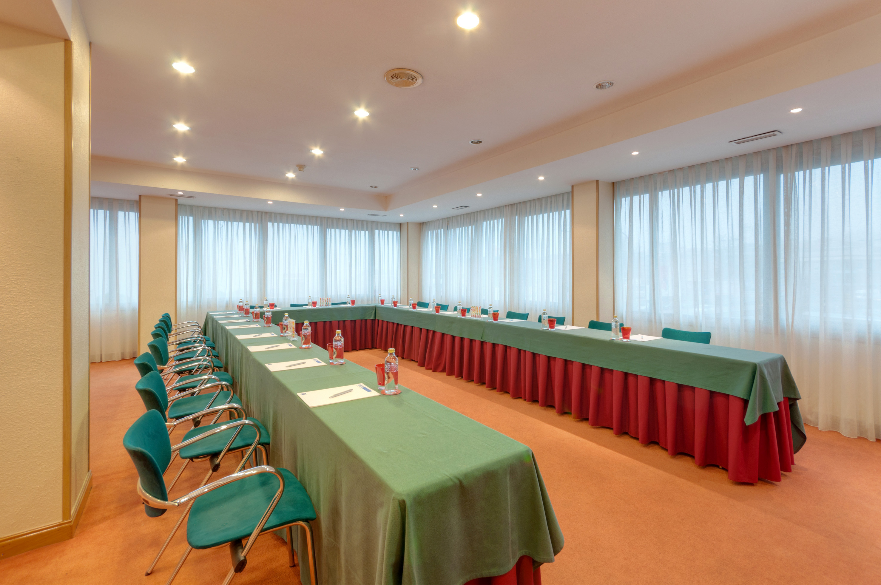 U-shaped conference room with green tables, teal chairs, and window light.