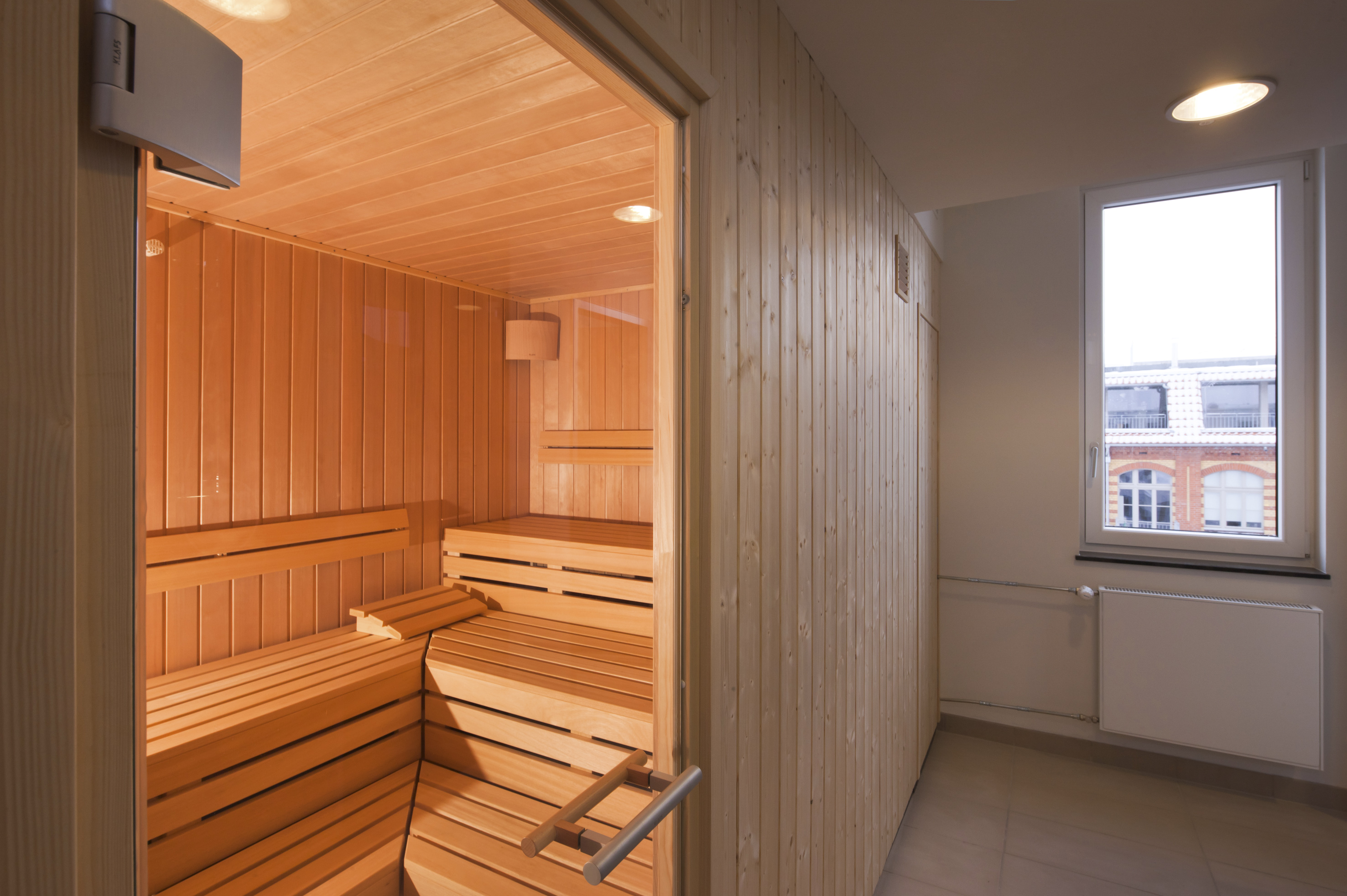 Wooden sauna interior with warm lighting, tiered benches, next to a window.