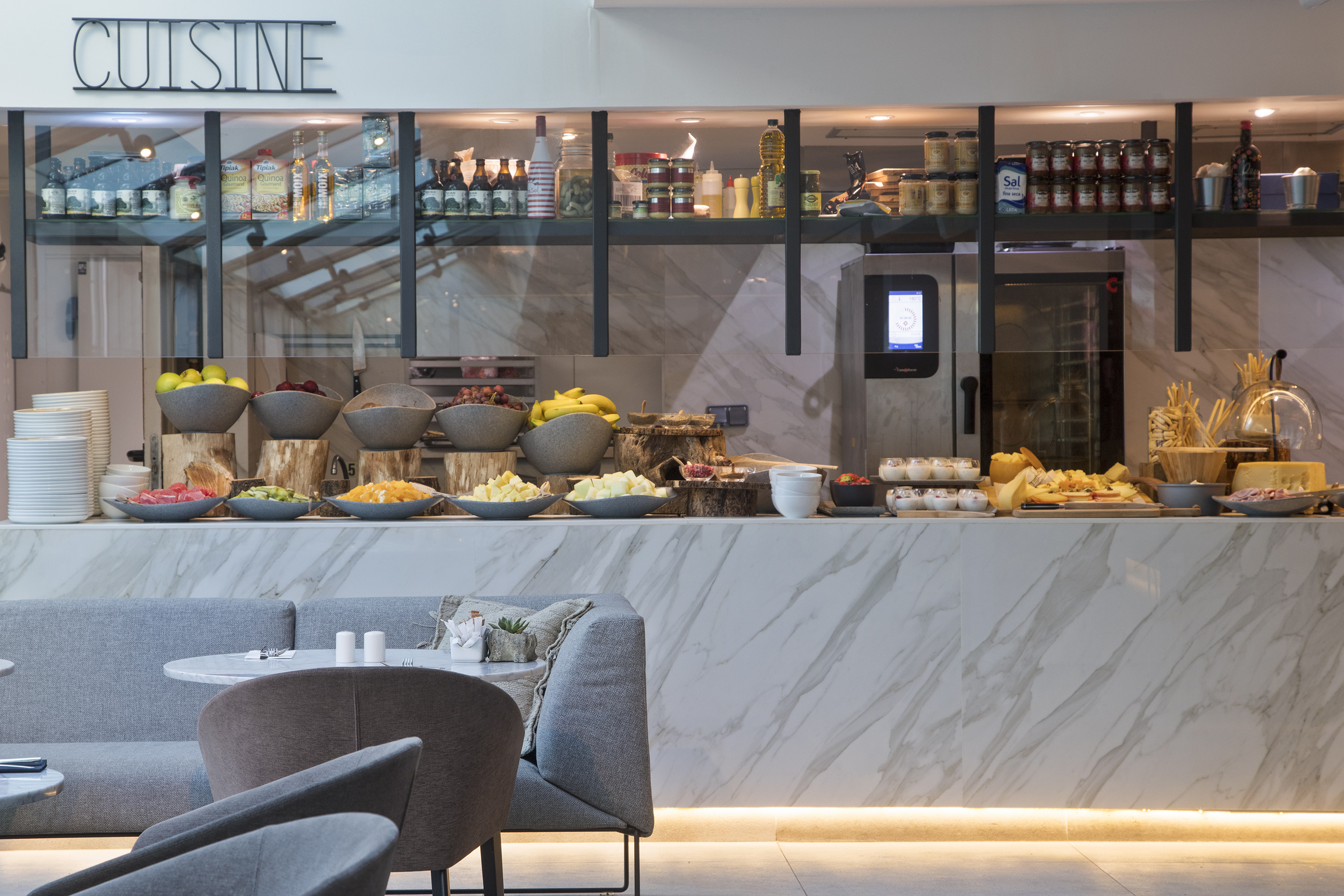 Hotel buffet with fresh fruit, cheese, deli meats, and 'Cuisine' sign.