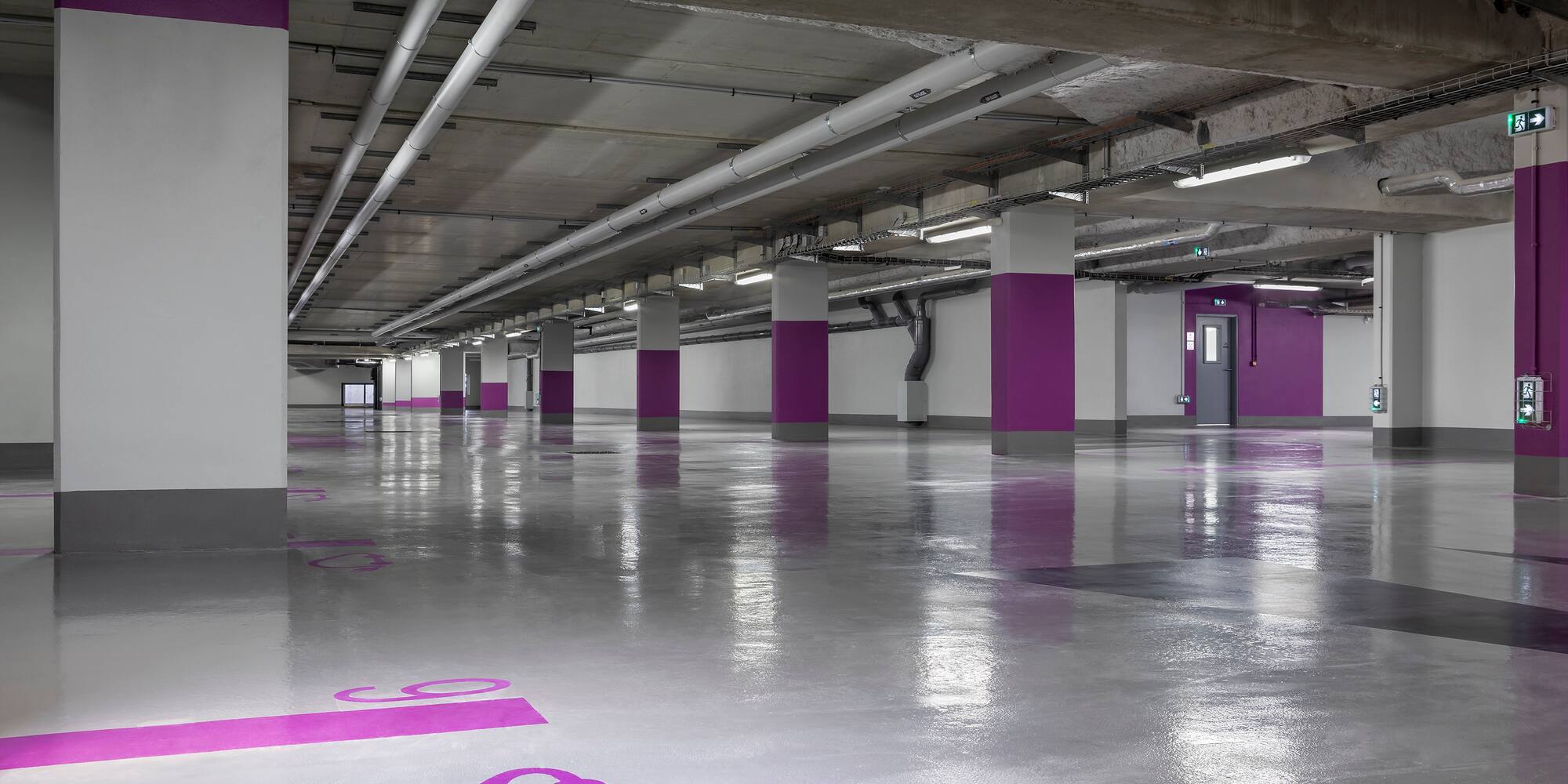Modern, empty underground parking garage with purple EV charging symbols.