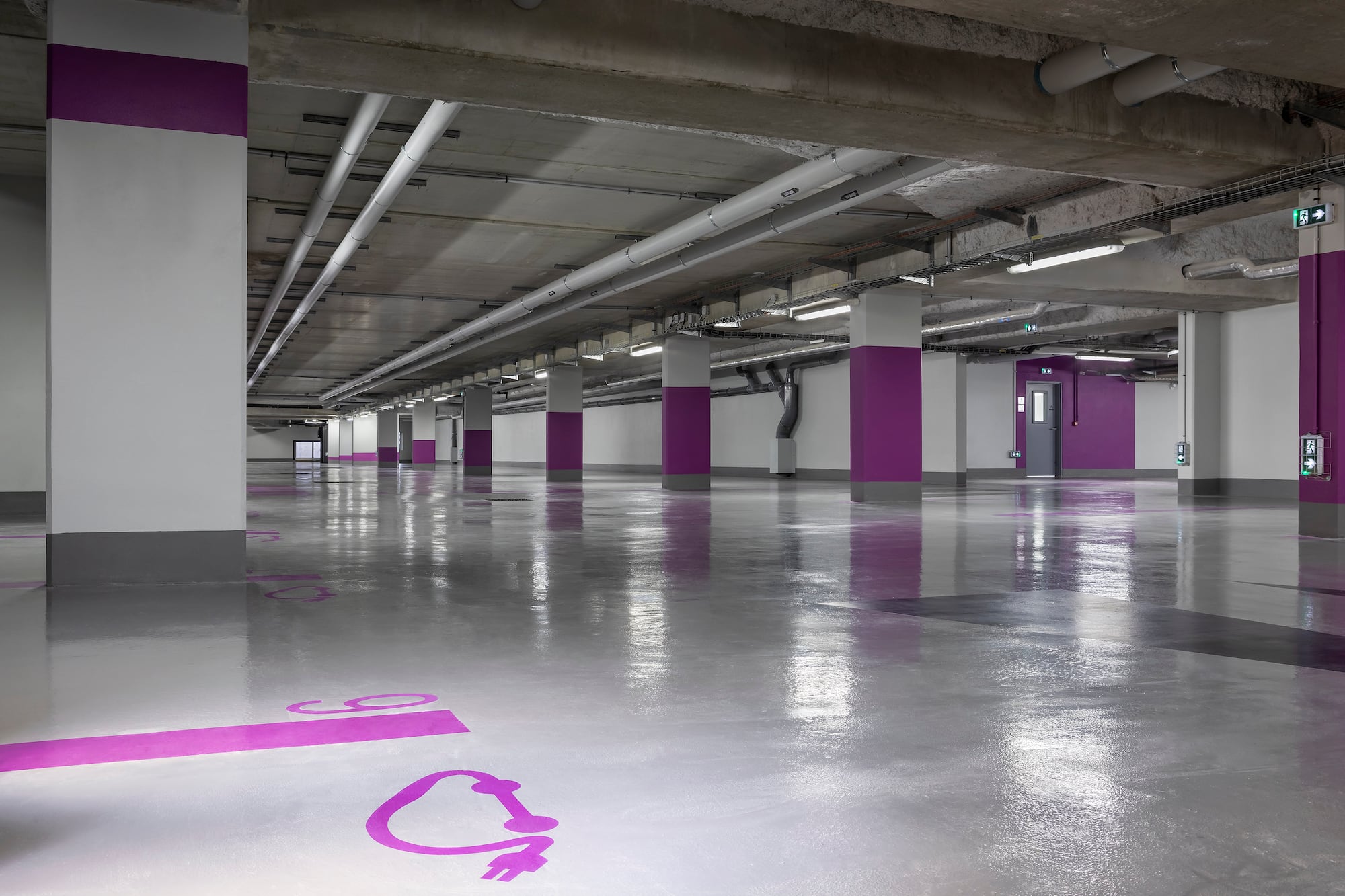 Modern, empty underground parking garage with purple EV charging symbols.