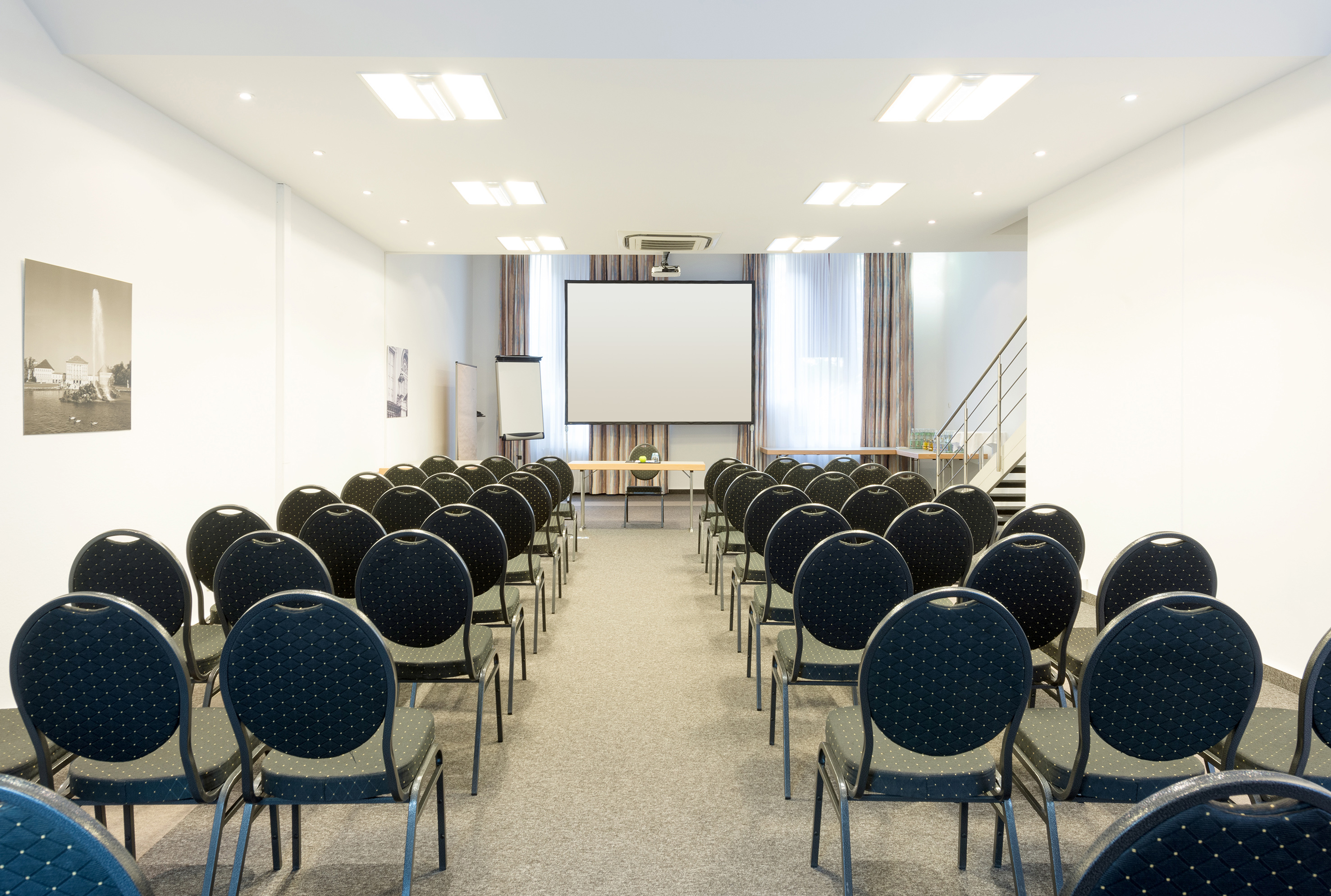 Empty conference room setup with chairs, projection screen, and flip chart.