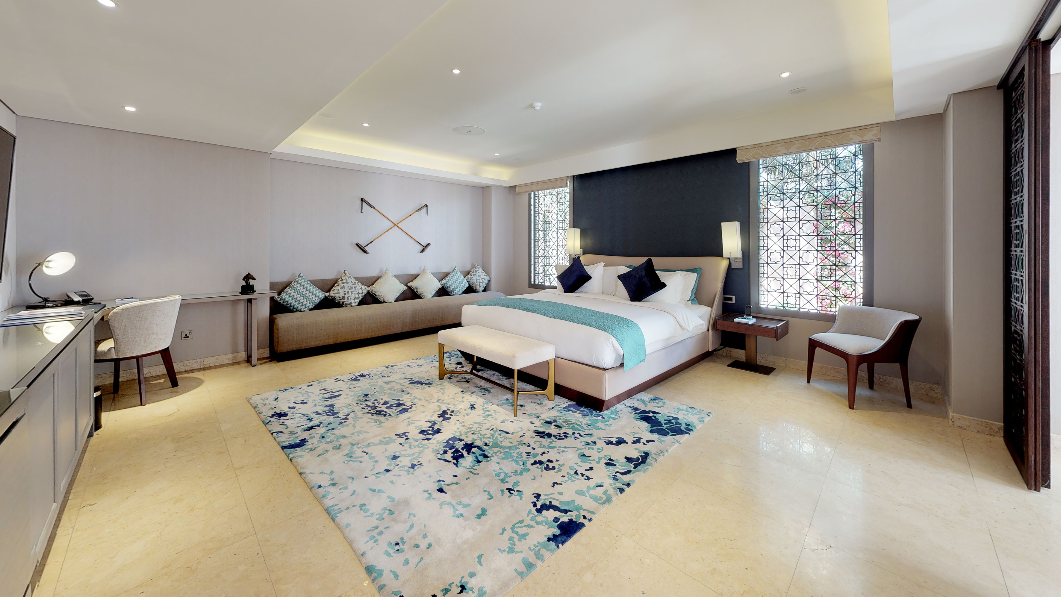 Modern luxury hotel bedroom with king bed, sofa, blue rug, and desk.
