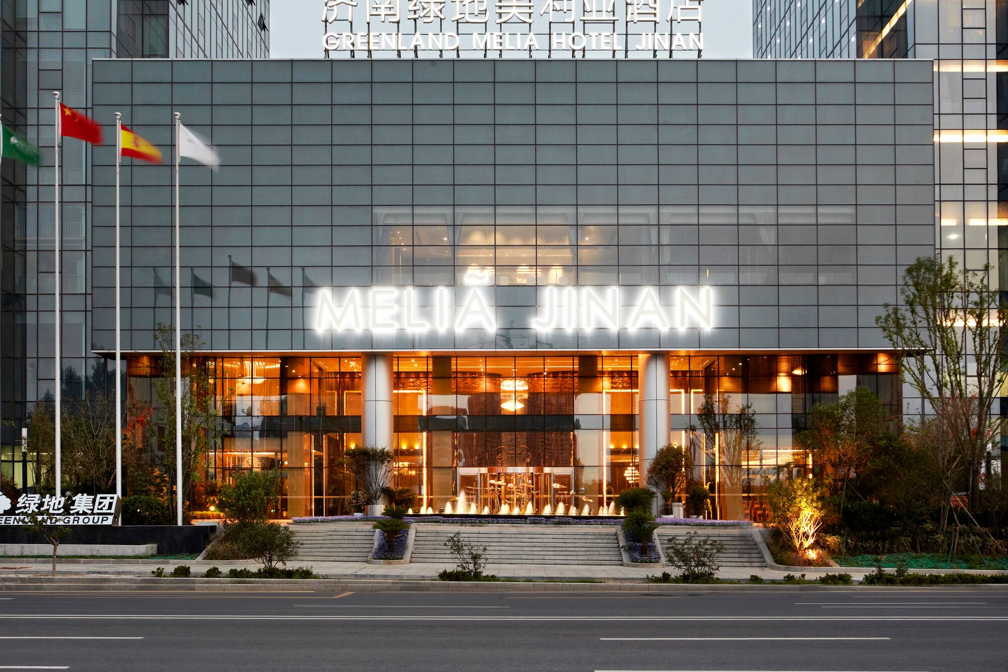 Greenland Melia Hotel Jinan facade with illuminated sign, flags, and fountain.