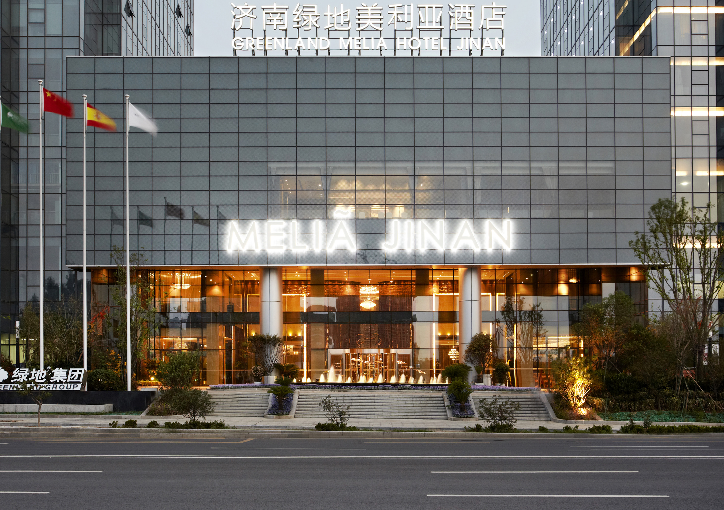 Greenland Melia Hotel Jinan facade with illuminated sign, flags, and fountain.
