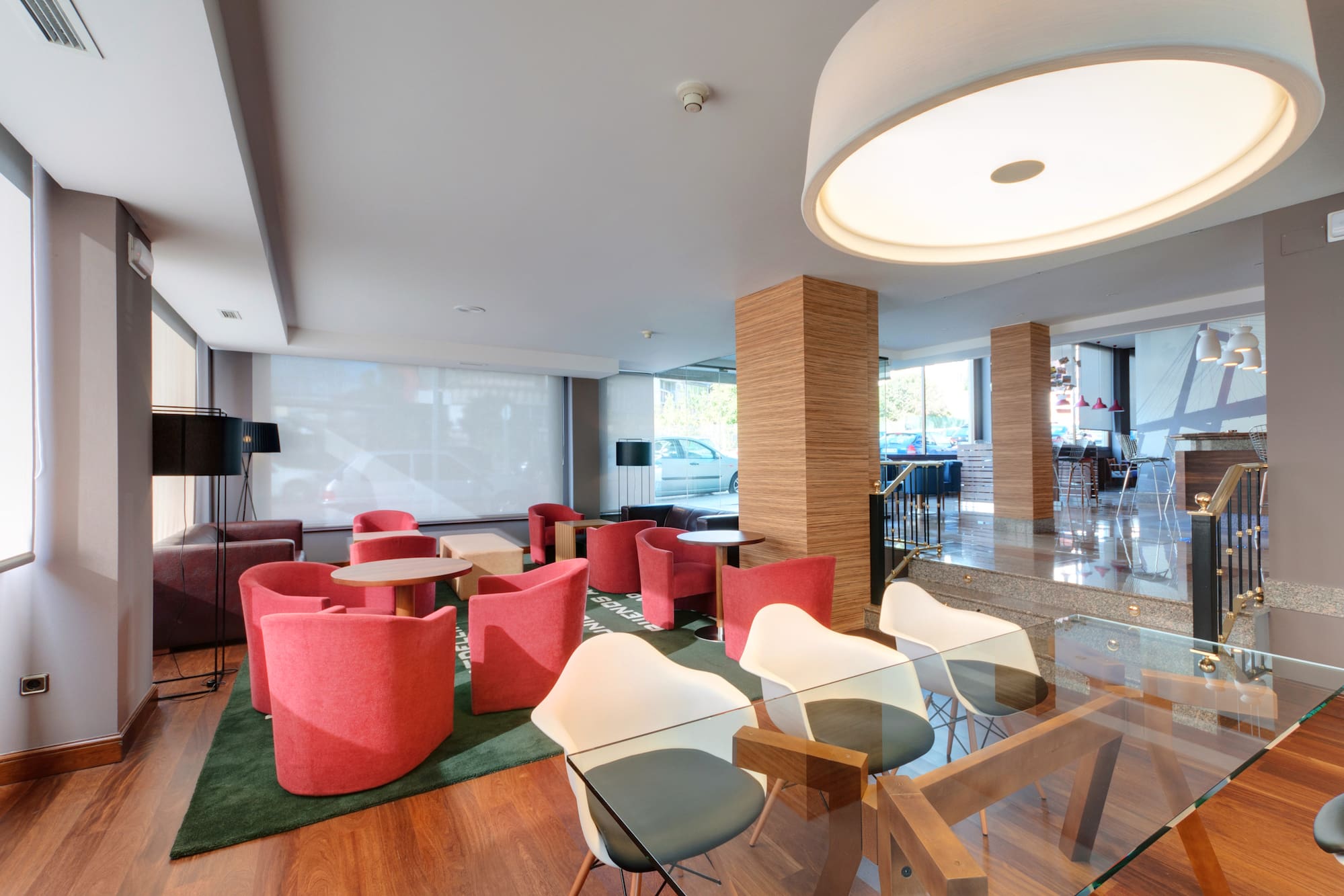 Modern hotel lobby with red armchairs, wooden flooring, and a bright lounge area.