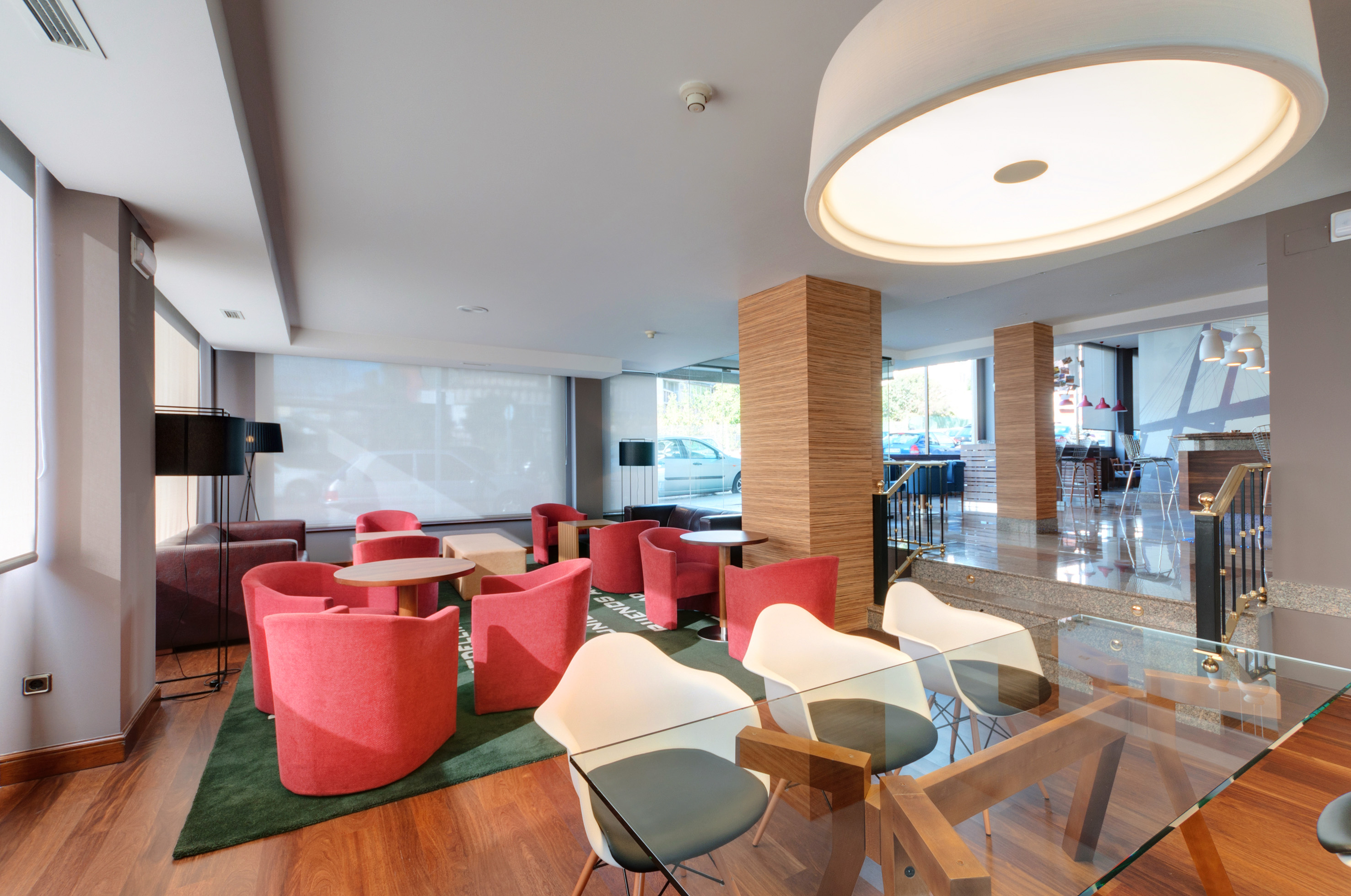 Modern hotel lobby with red armchairs, wooden flooring, and a bright lounge area.