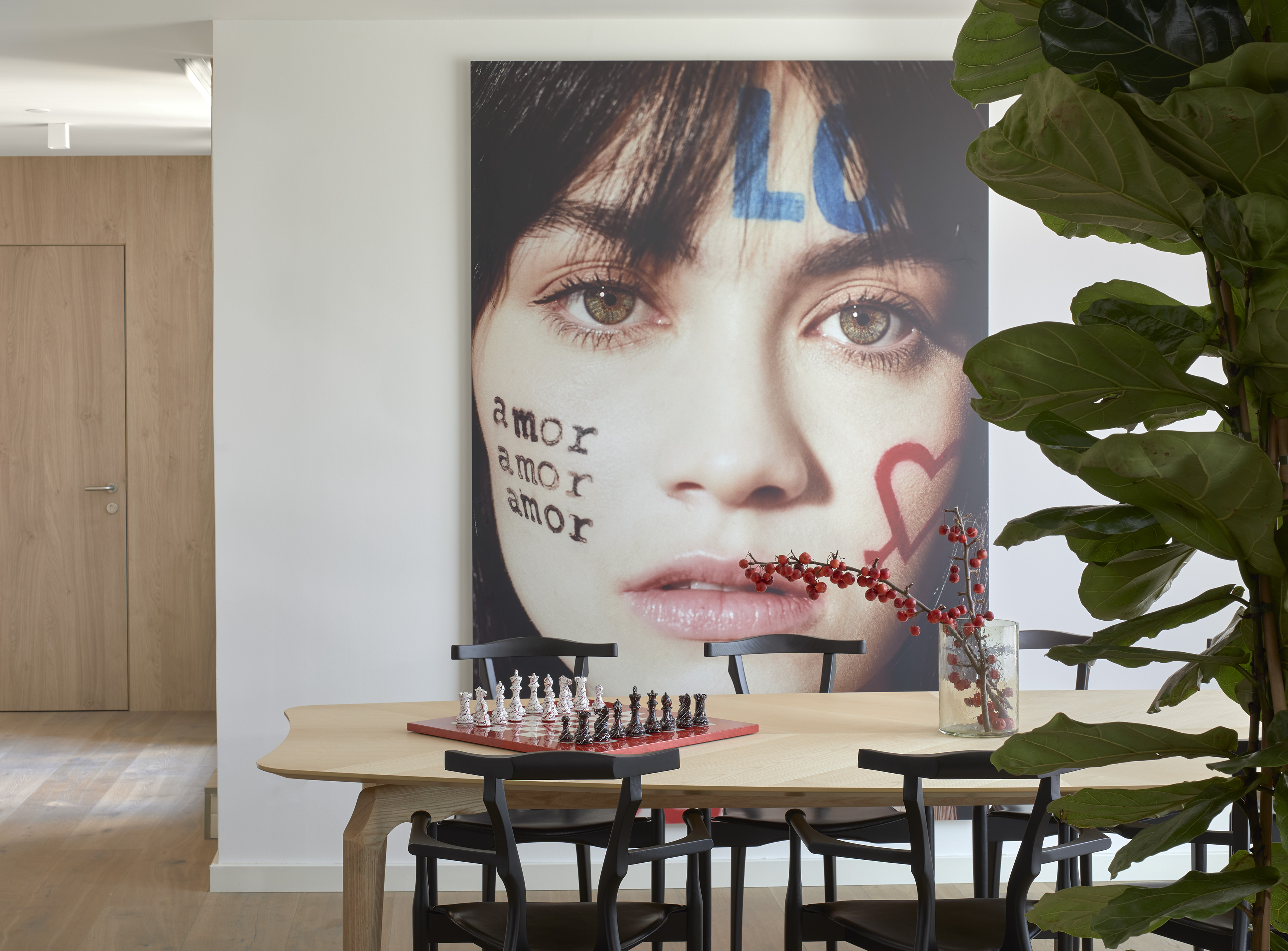 Modern dining room with large woman's face art, wood table, and chess set.
