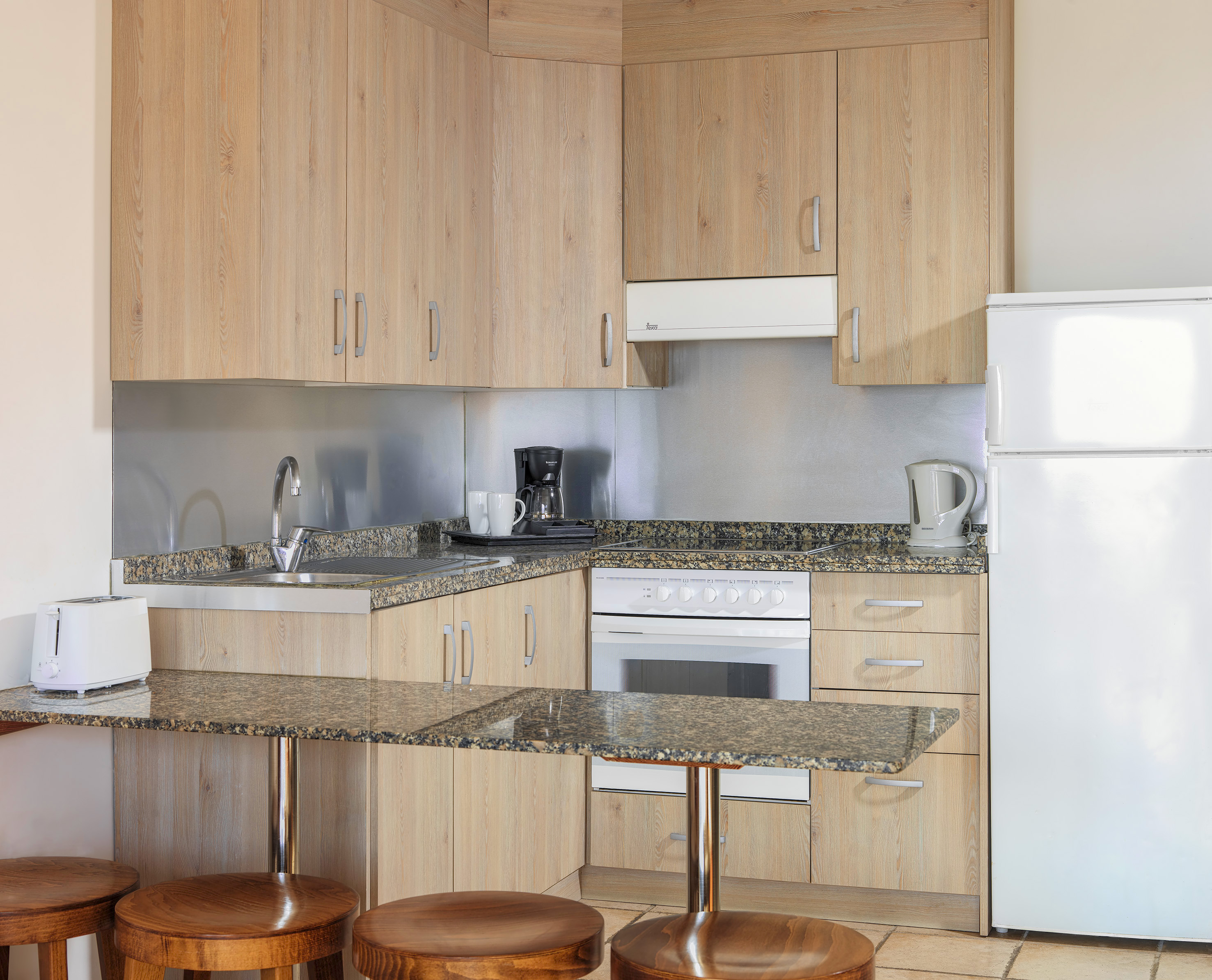 Compact kitchen: light wood cabinets, granite counters, white appliances, breakfast bar.