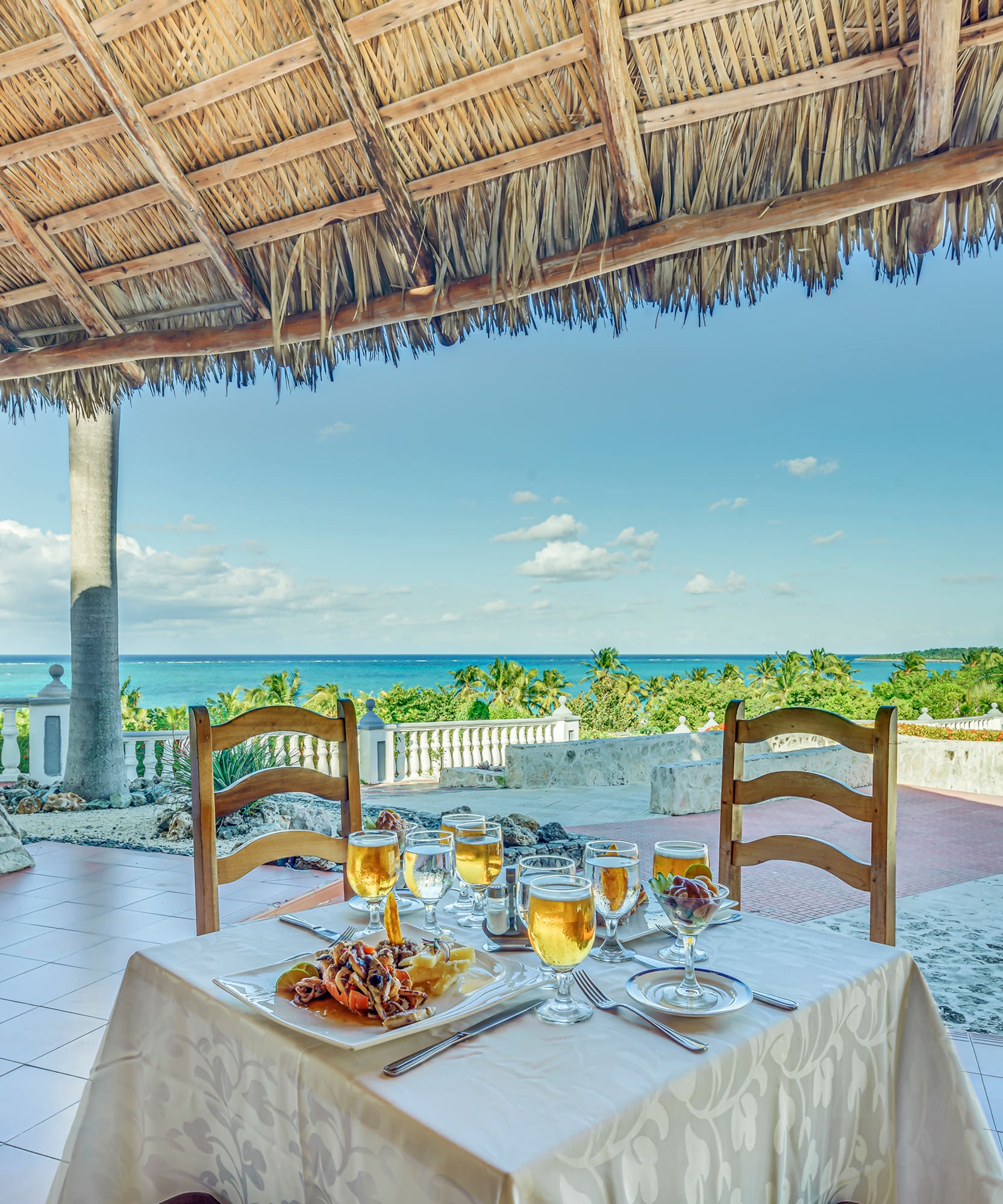 a table set for a dinner with a straw roof and a beach view