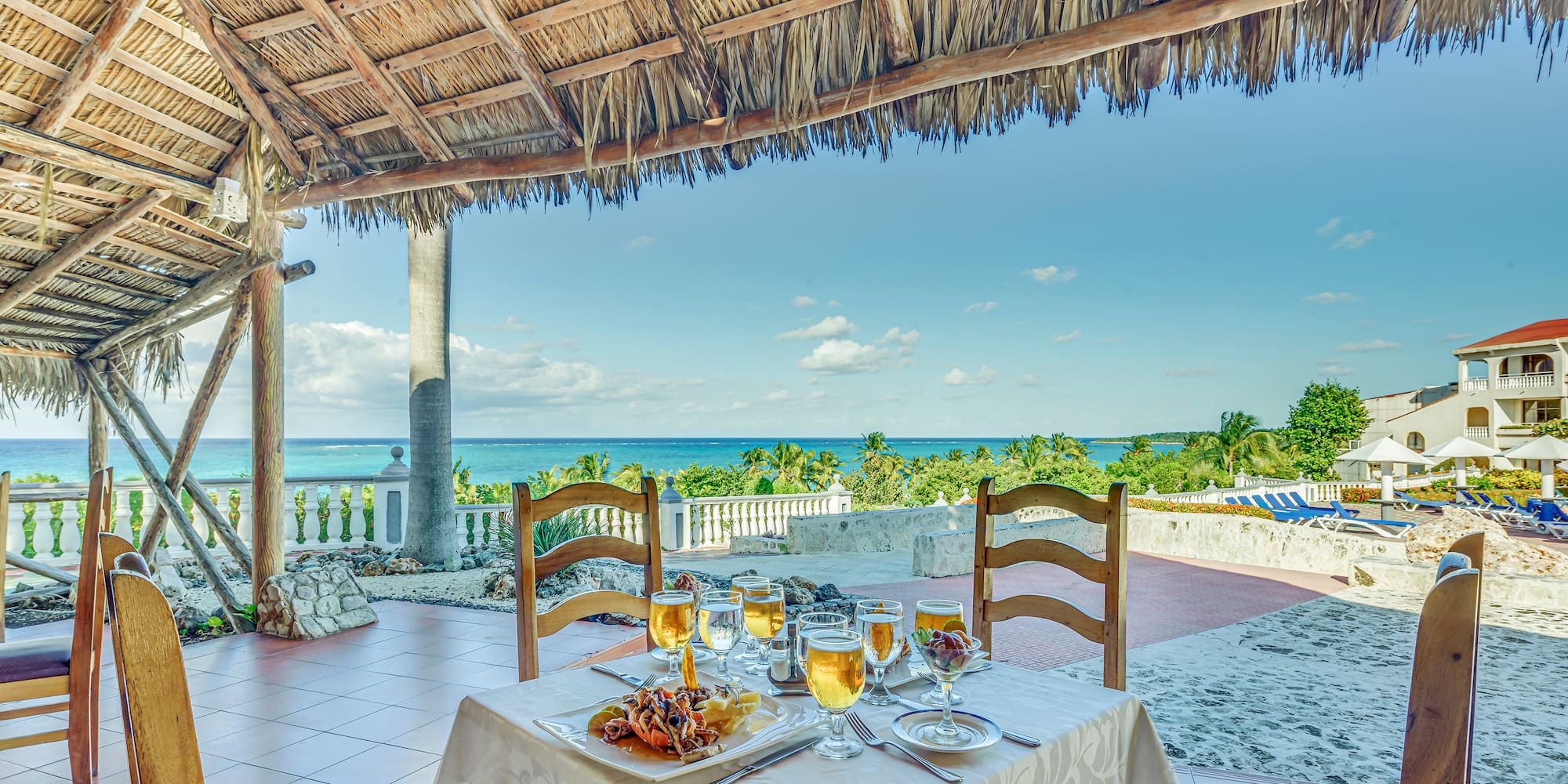 a table set for a dinner with a straw roof and a beach view