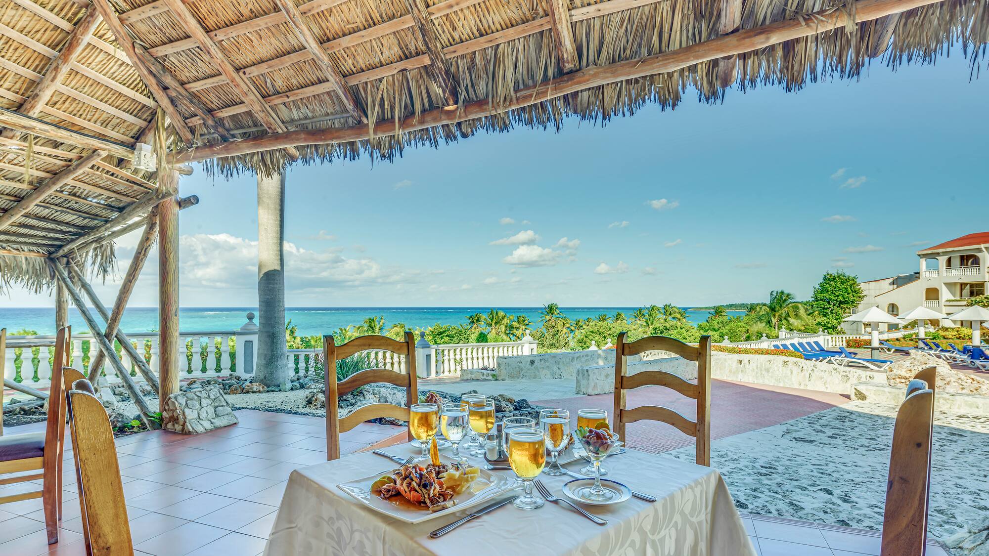 a table set for a dinner with a straw roof and a beach view