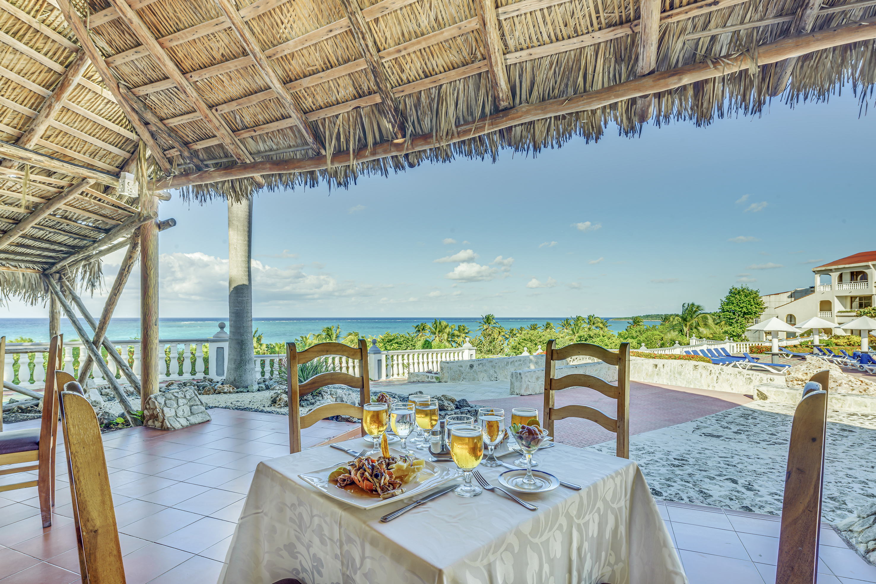 a table set for a dinner with a straw roof and a beach view