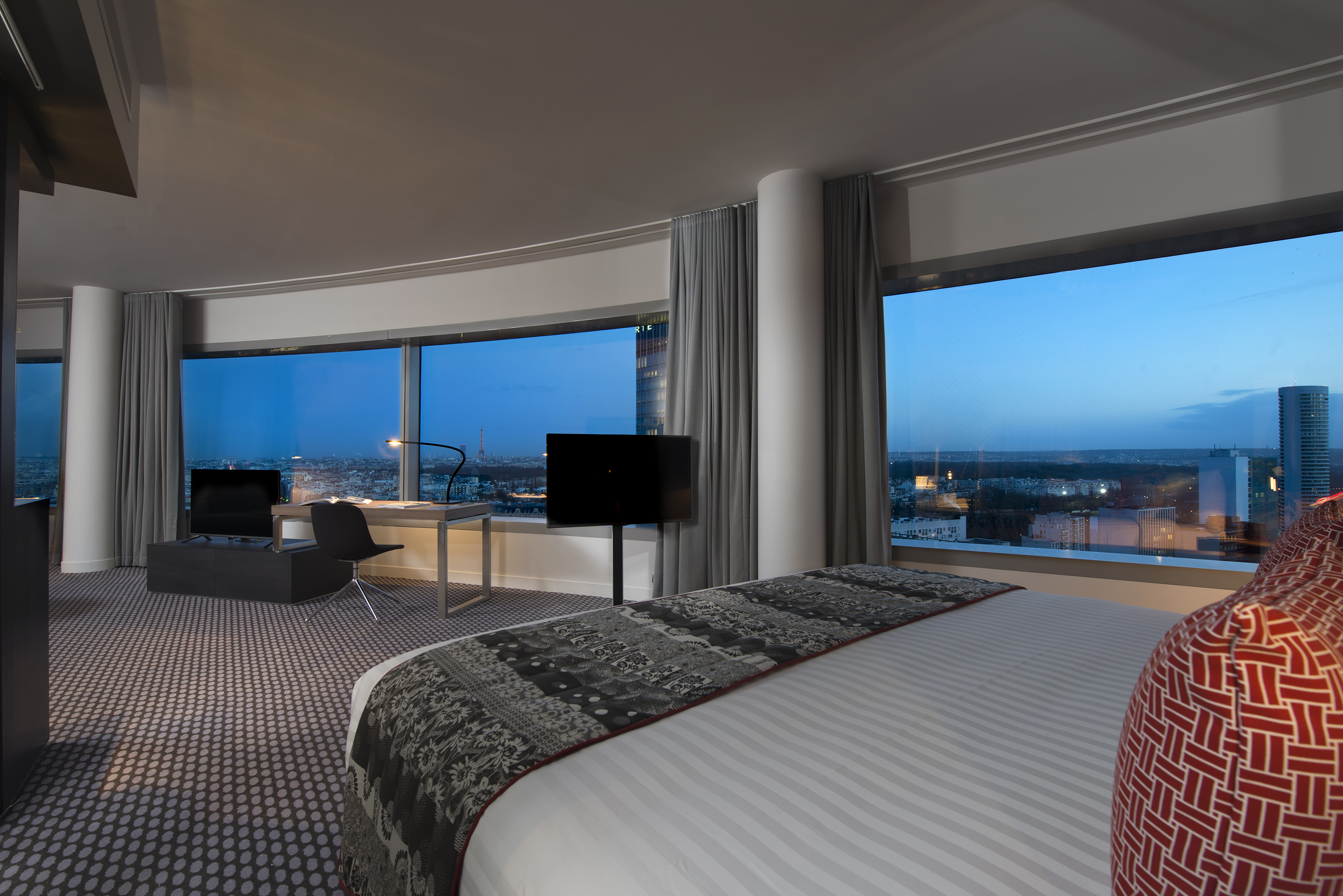 Modern hotel bedroom with panoramic Paris skyline view at night.