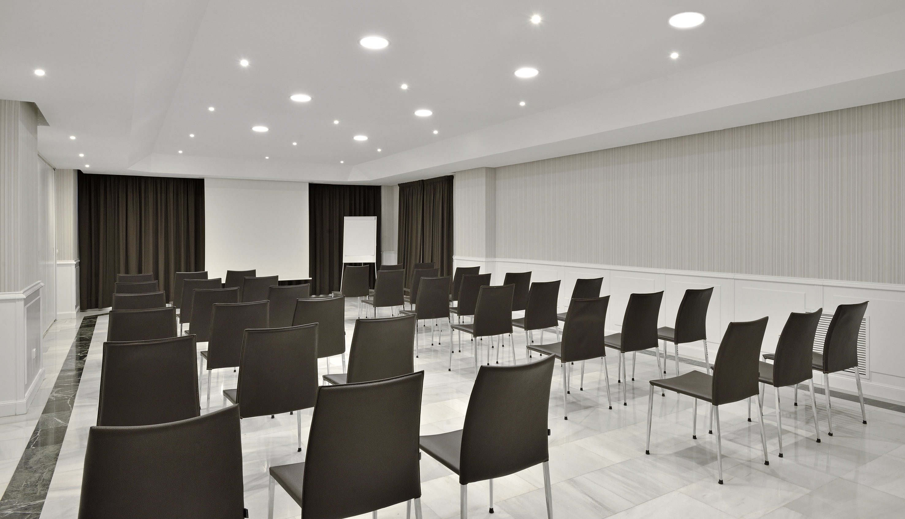 Modern conference room with dark chairs, marble floor, and white screen.