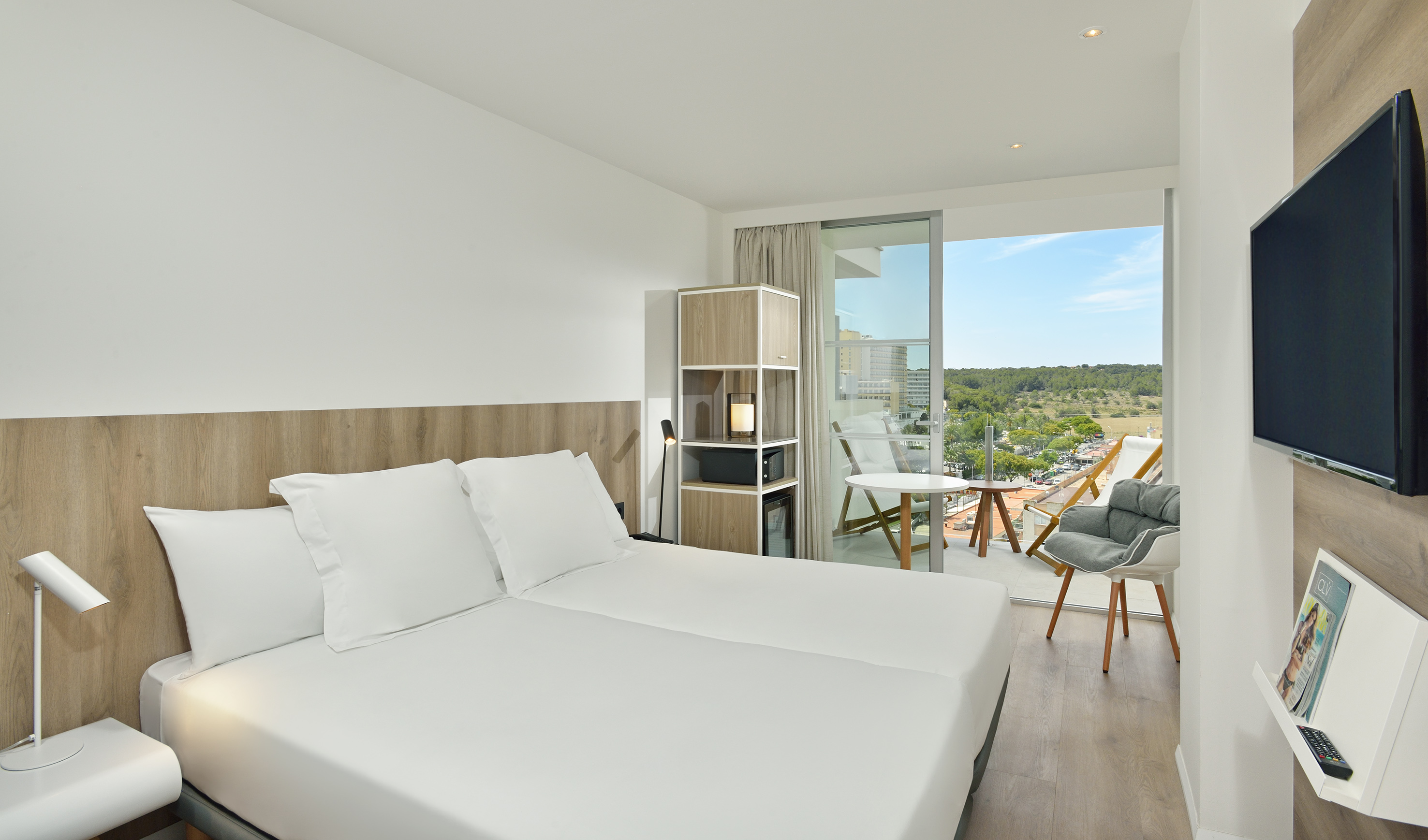 Modern hotel room with white bed, balcony, and scenic resort view.