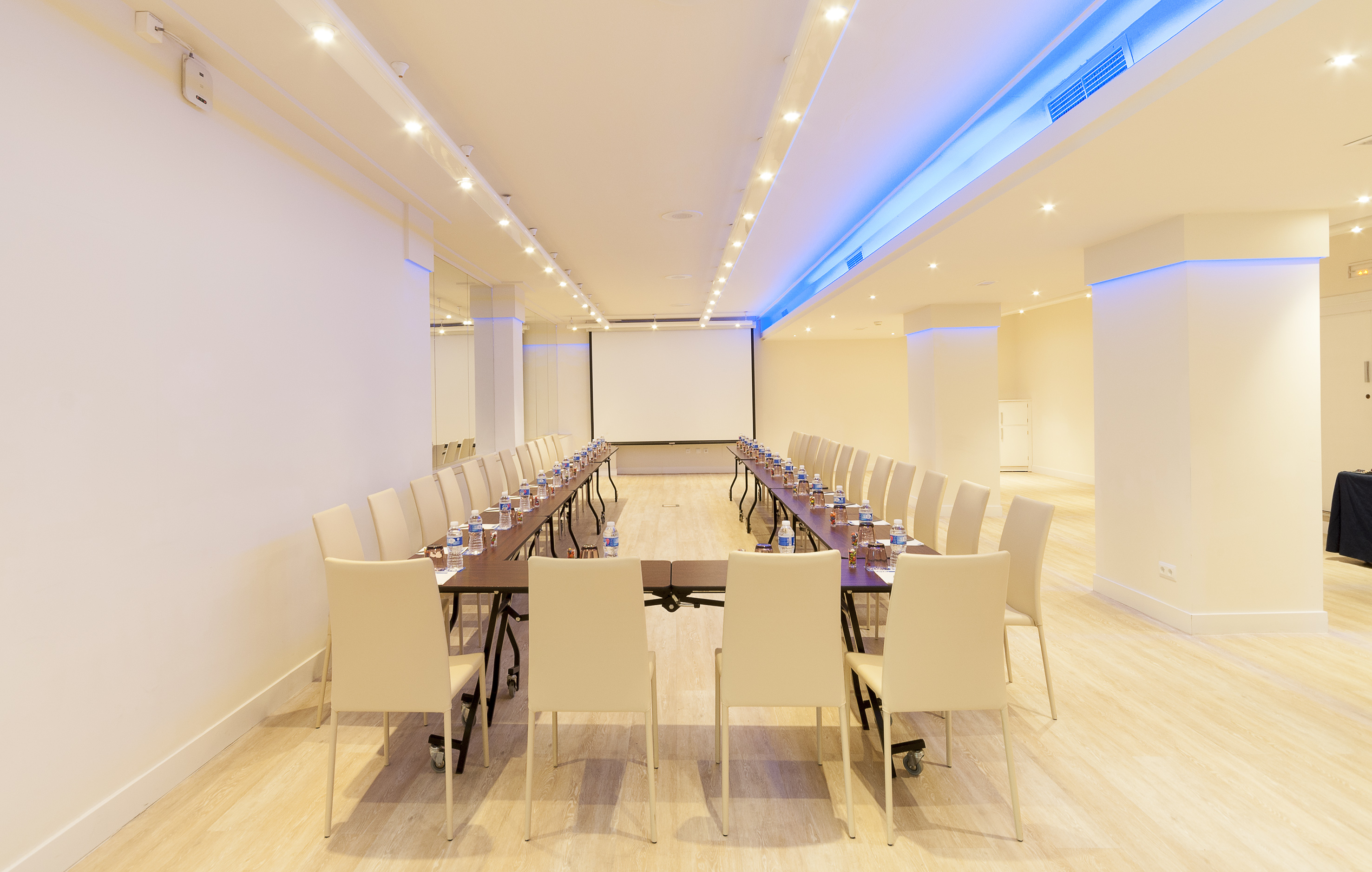 U-shaped meeting room setup with projector screen and blue ambient lighting.