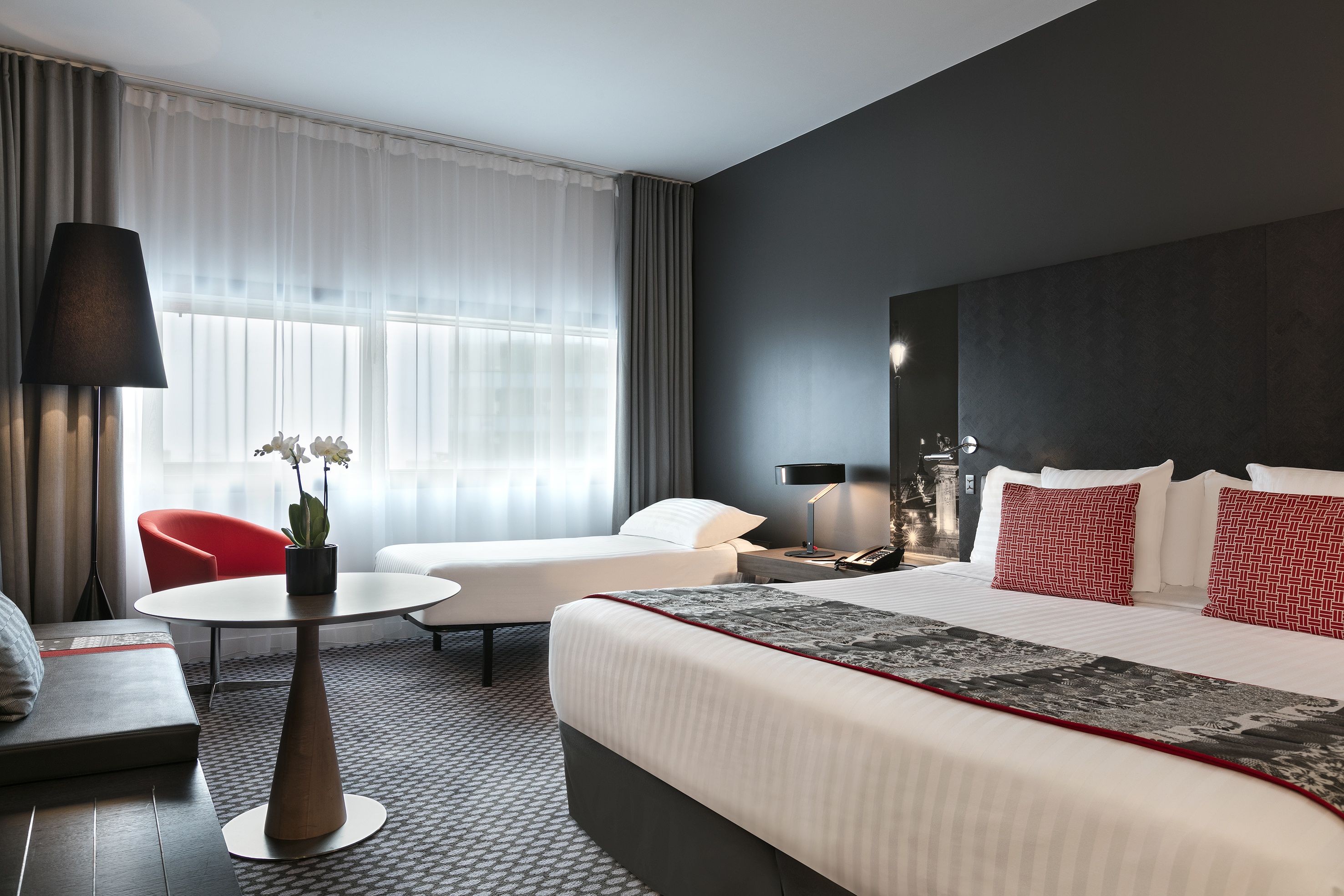 Stylish hotel room featuring a king bed, twin bed, red accent chair, and modern decor.
